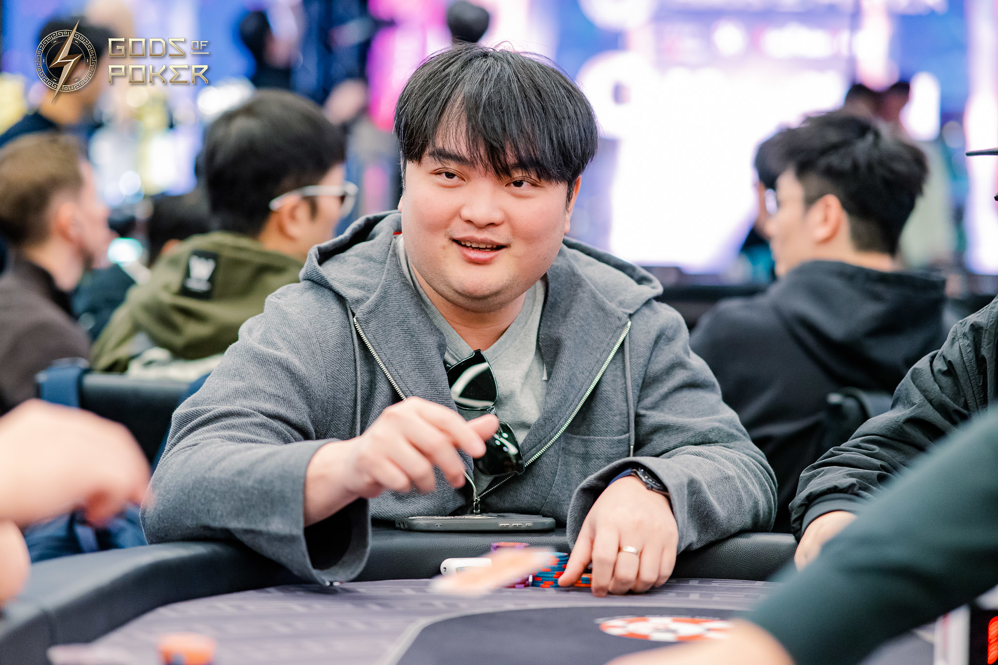 Man holding poker chips at a poker table, smiling slightly during a game.