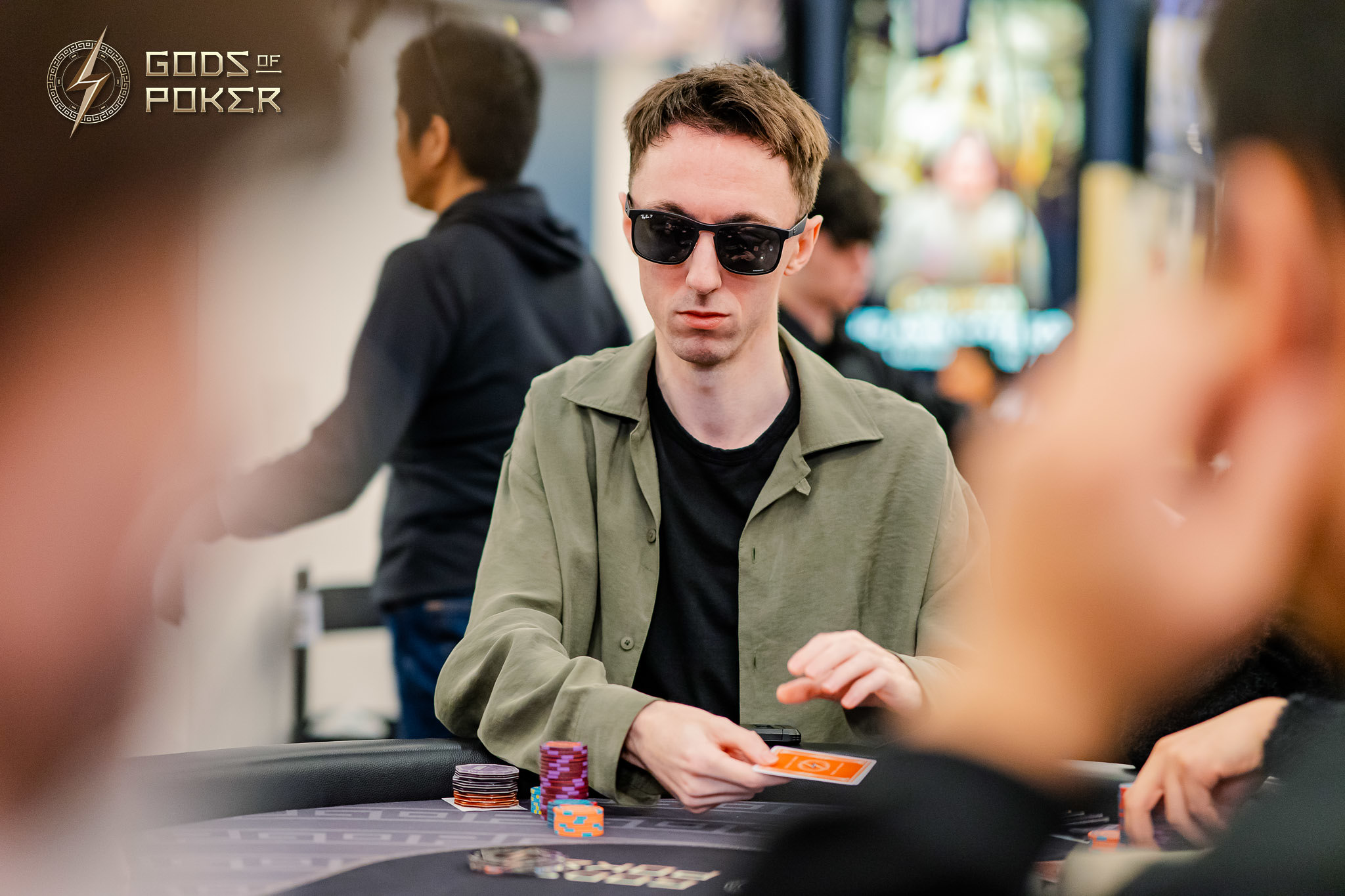 Man in sunglasses at a poker table, holding cards during a game.
