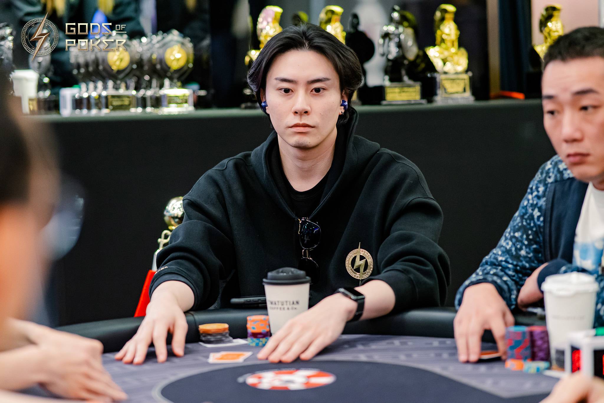 Young Asian man in black hoodie with serious expression playing poker at a table.
