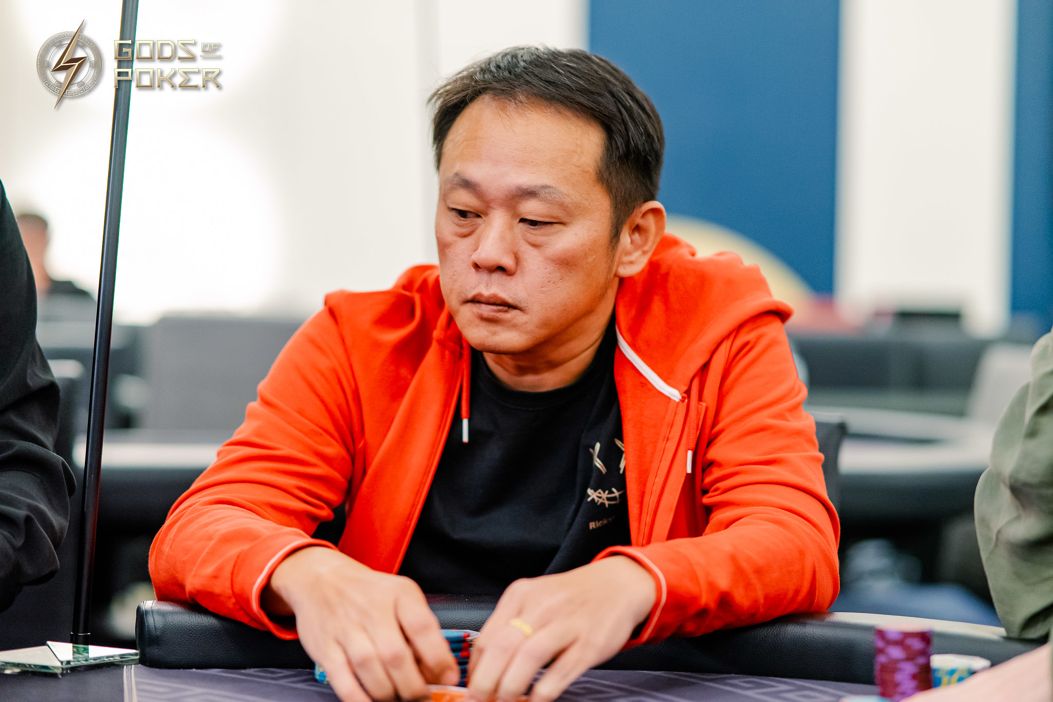 A man in a bright orange jacket intently playing poker at a table.