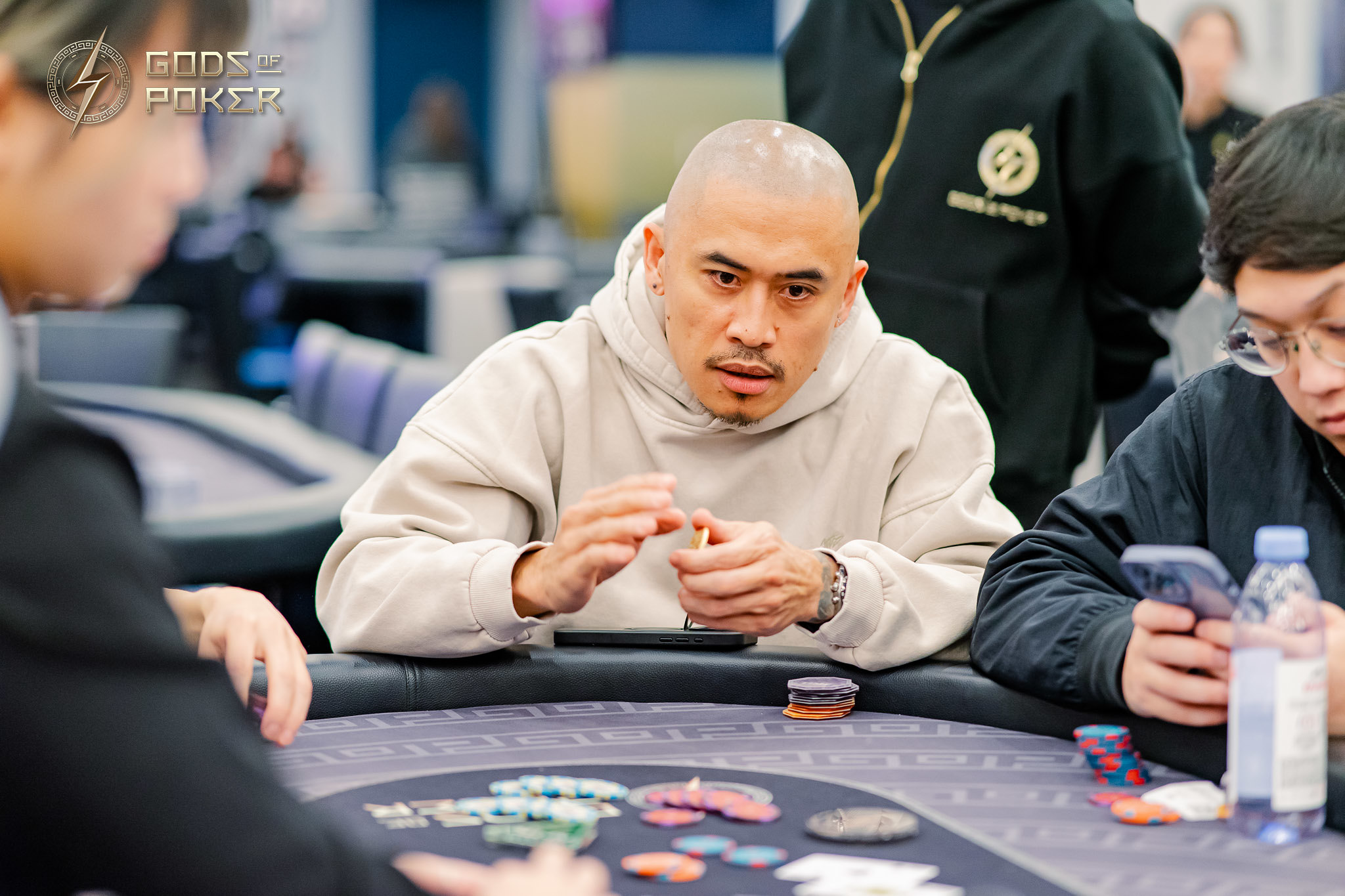 A man with a shaved head intently focuses on his cards at a poker table.