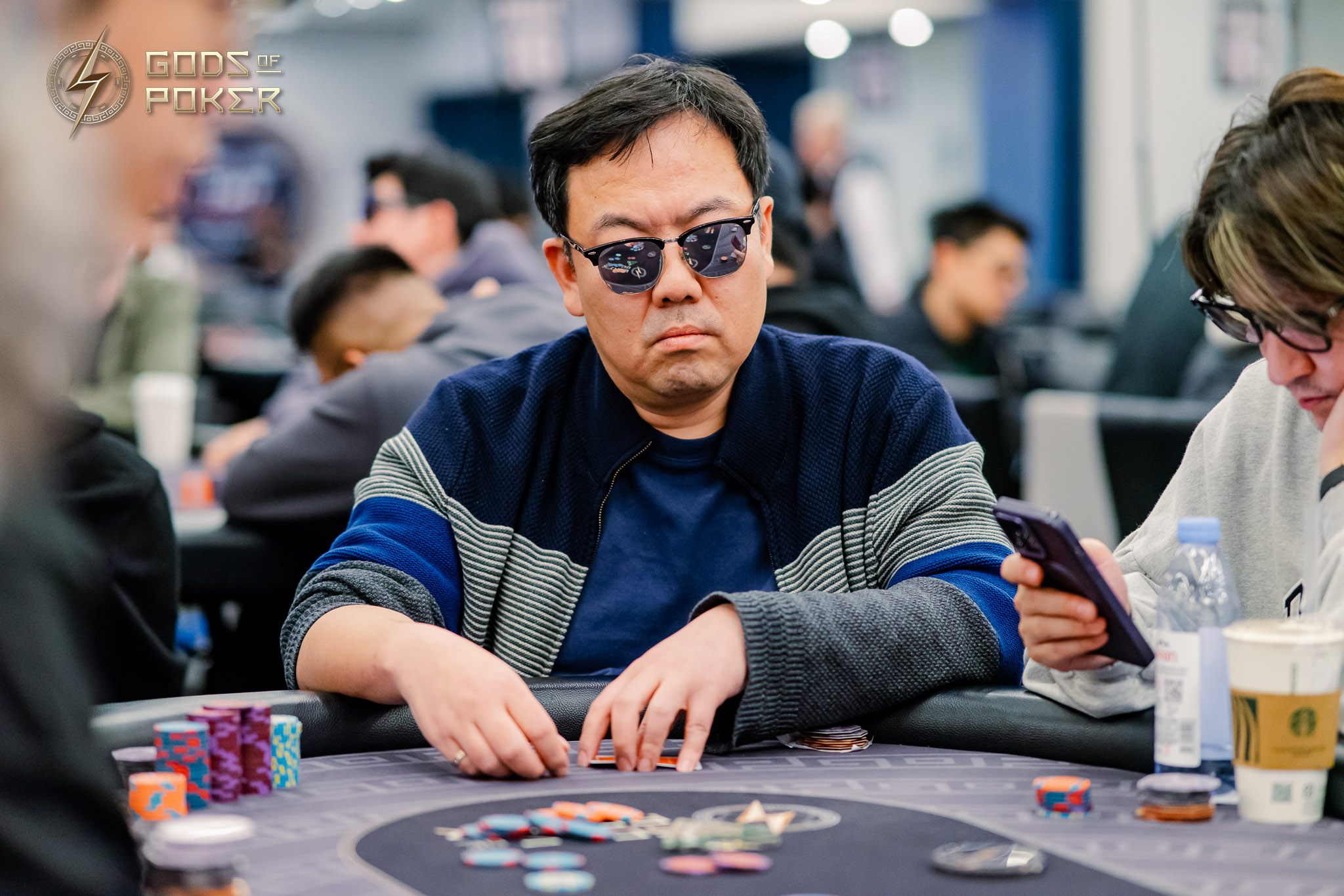 Man in sunglasses and blue-grey sweater intensely playing poker at a casino table.