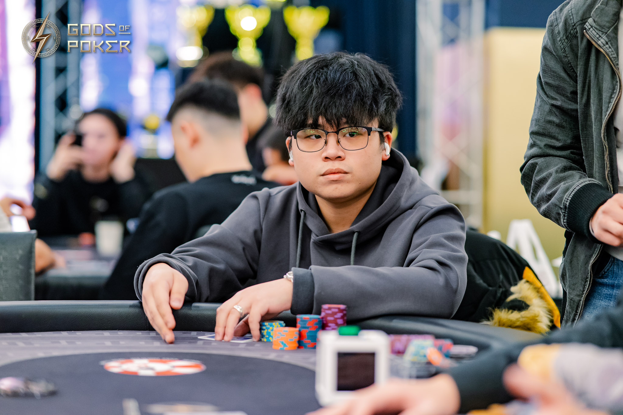 Young man in glasses and gray hoodie intensely focused at a poker table with chips.