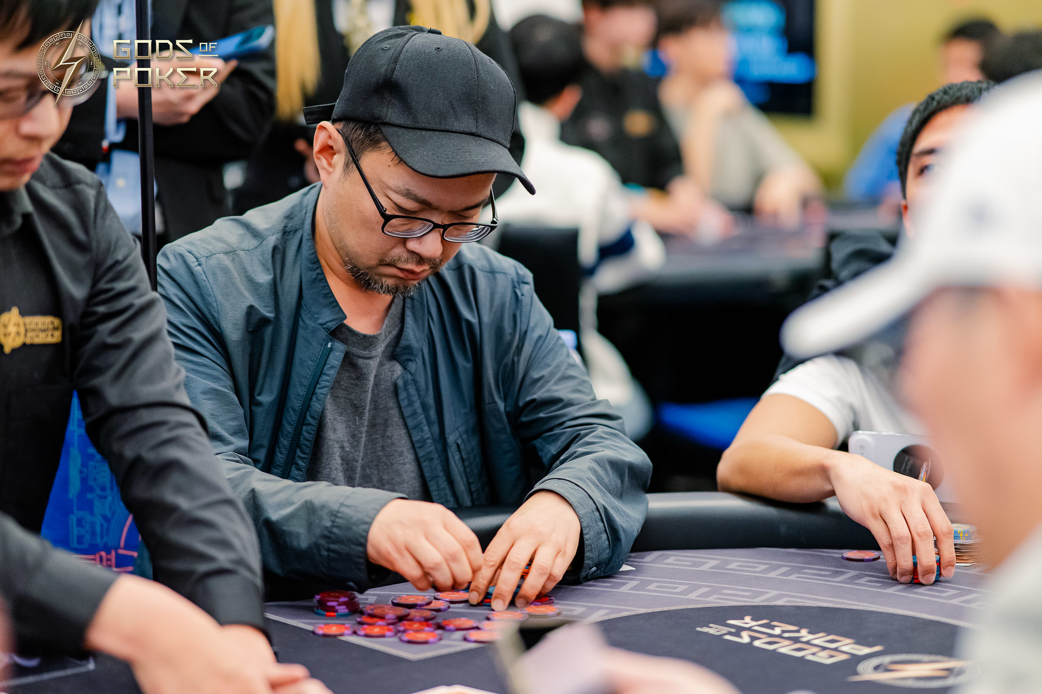 Man in black cap and glasses carefully moving red poker chips at a table.