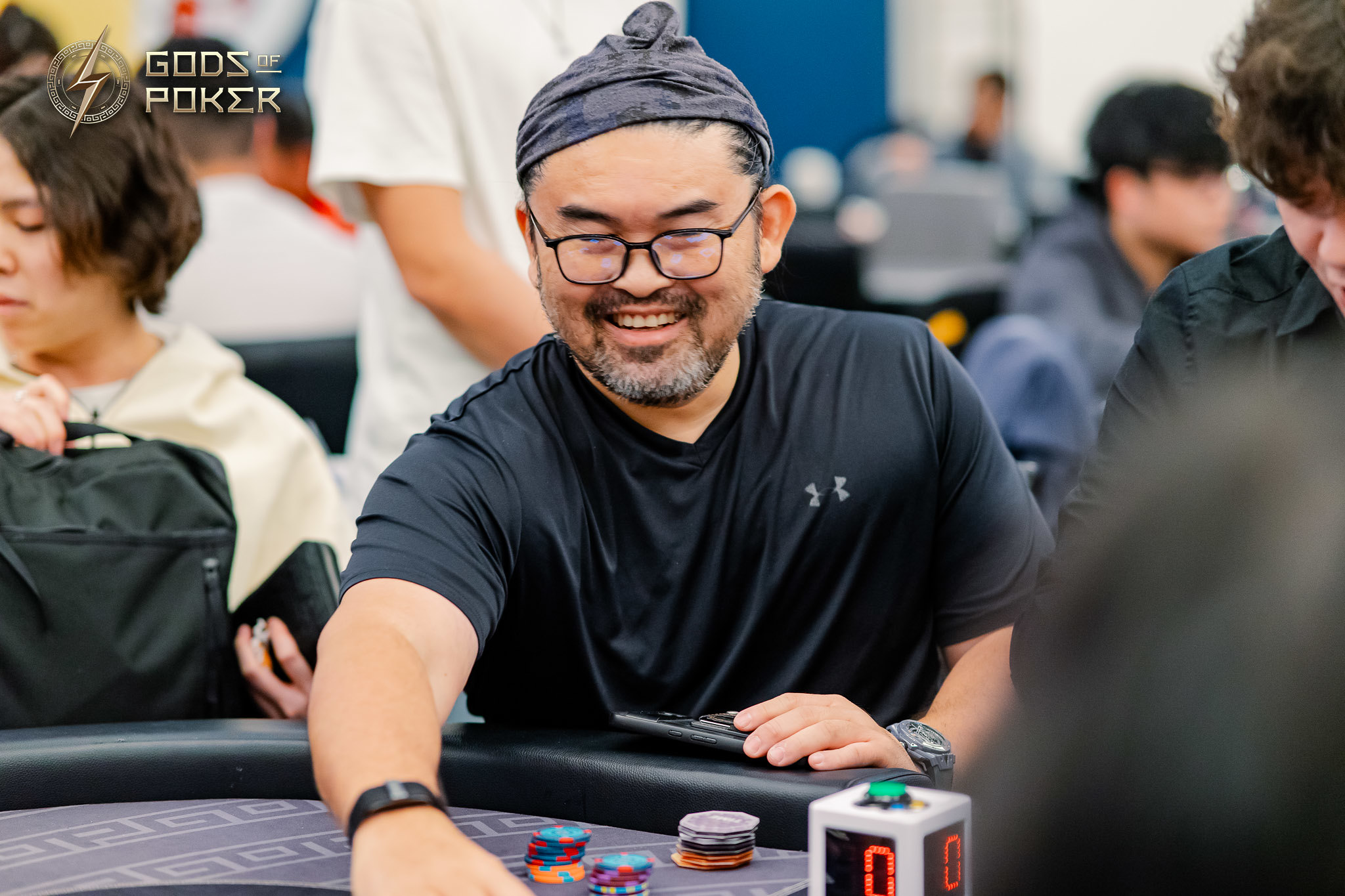 Smiling man wearing a beanie and glasses playing poker, reaching for chips.