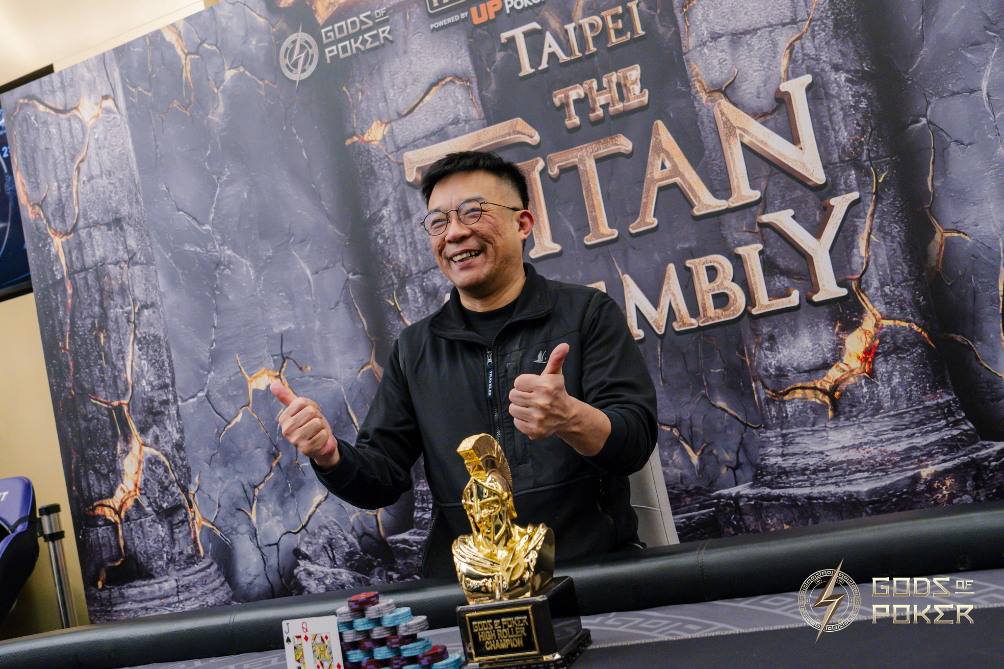 Happy man gives two thumbs up next to a gold poker trophy at an event.