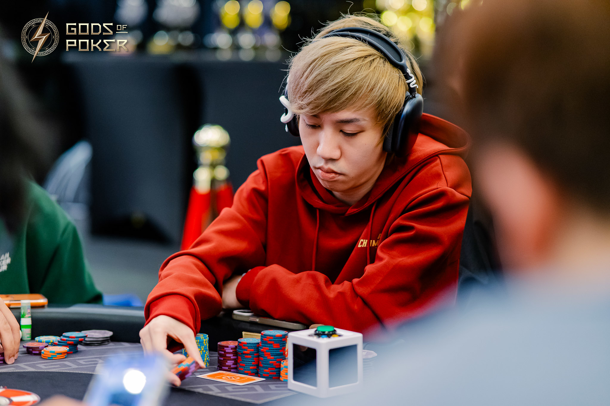 Young man in red hoodie and headphones concentrating at a poker table with chips.