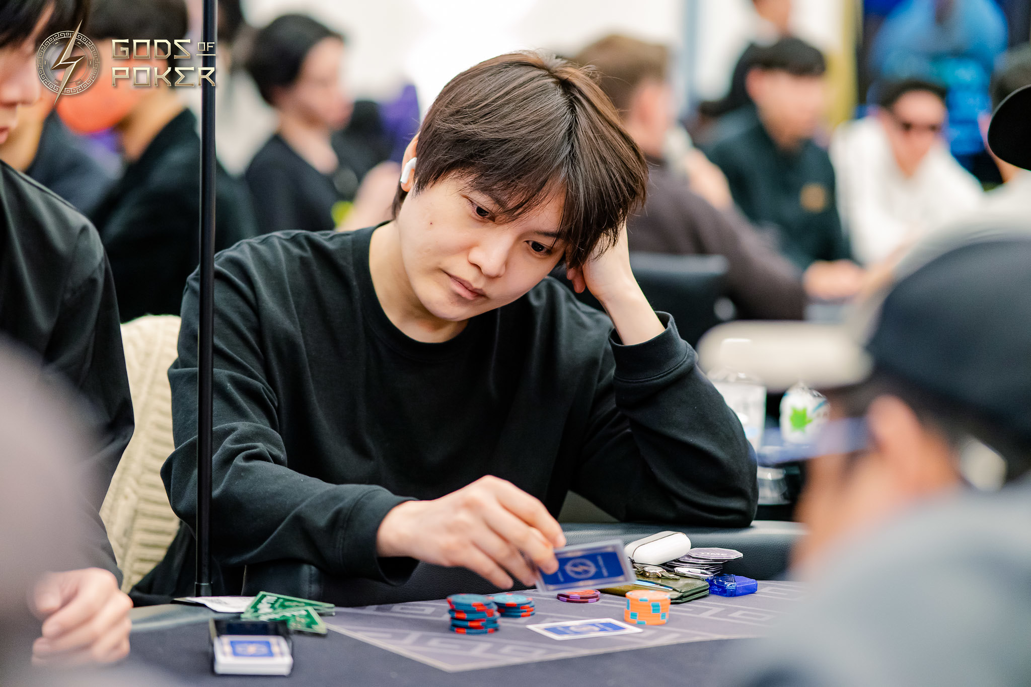 Poker player in a black shirt contemplates strategy at a table with chips and cards.