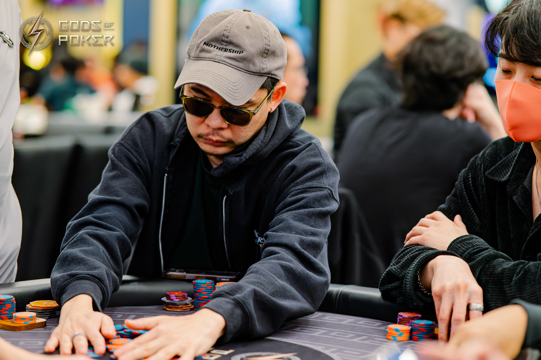 Man in cap and sunglasses playing poker, pushing chips on a table.
