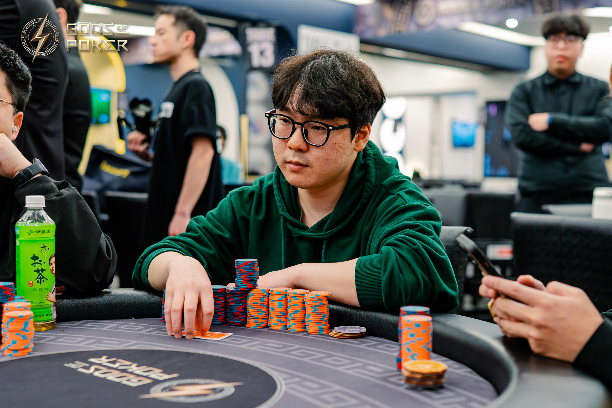 Young man with glasses and green hoodie playing poker at a table with chips.