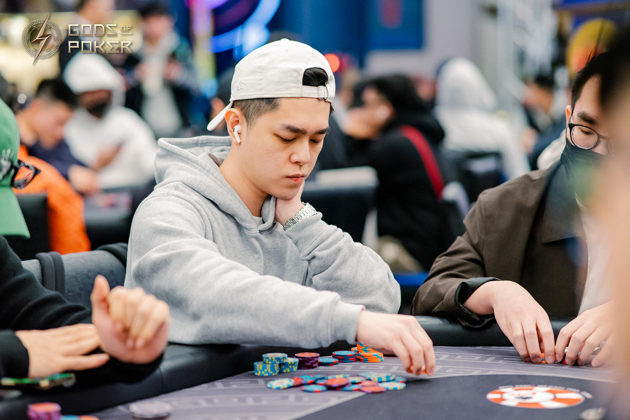 Man in a grey hoodie and white cap playing poker, moving colorful chips.