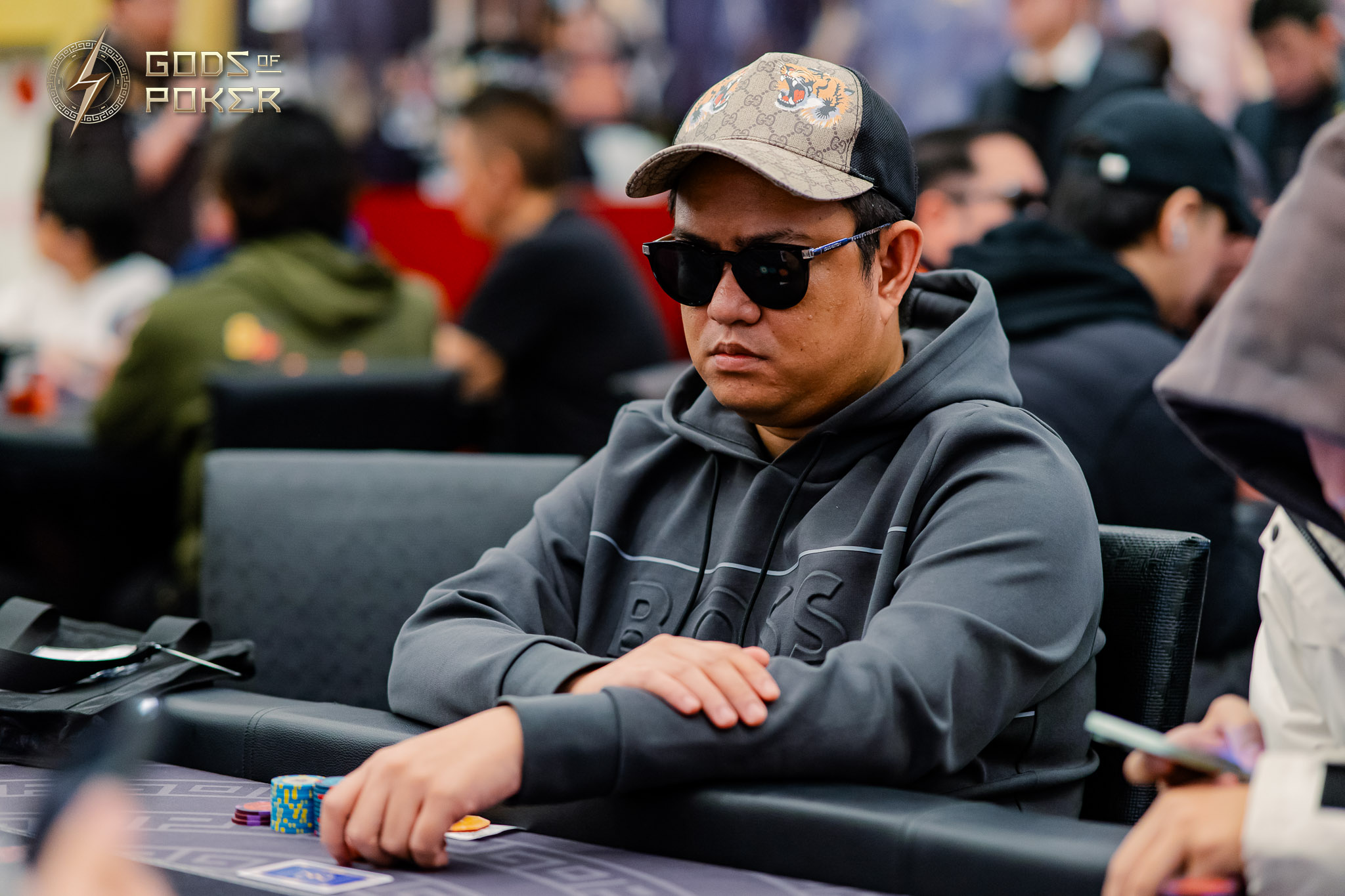 Man in a cap and sunglasses intently playing poker at a casino table.