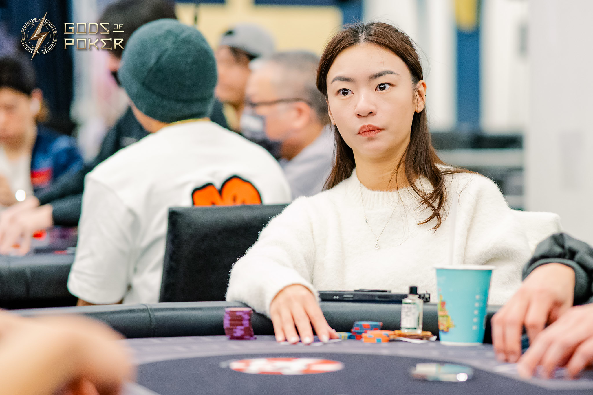 Young Asian woman sits intently at a poker table, with chips and a blue cup.