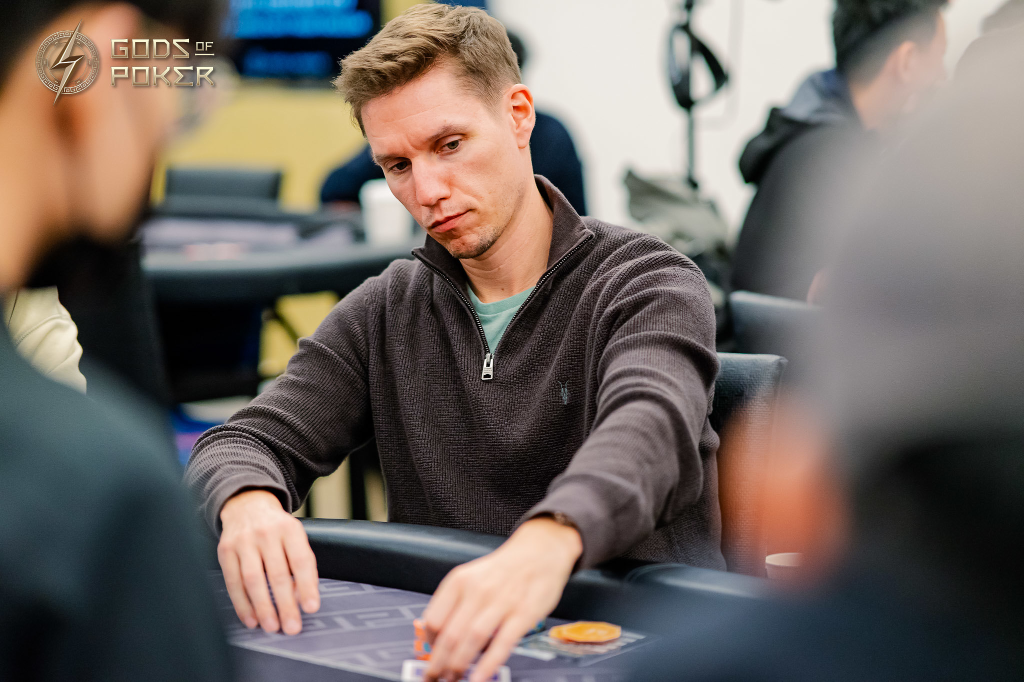 Man in brown sweater intently playing poker at a table with chips.