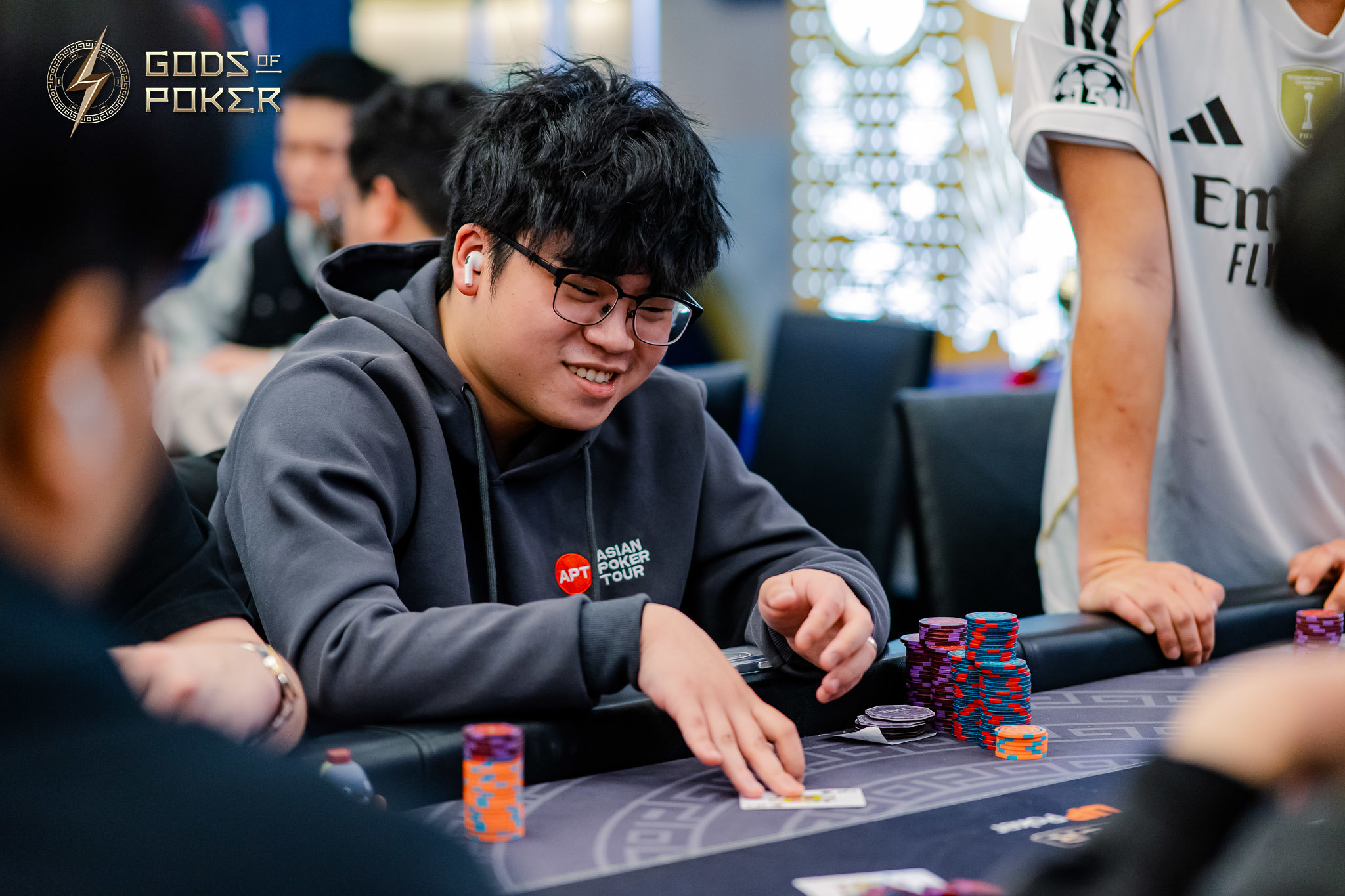 Young man with glasses smiling while playing poker at a table with chips.
