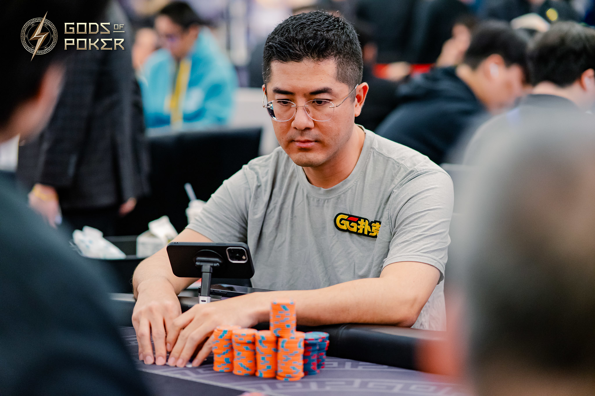 Man in grey Go88 shirt at a poker table with phone and stacked chips.