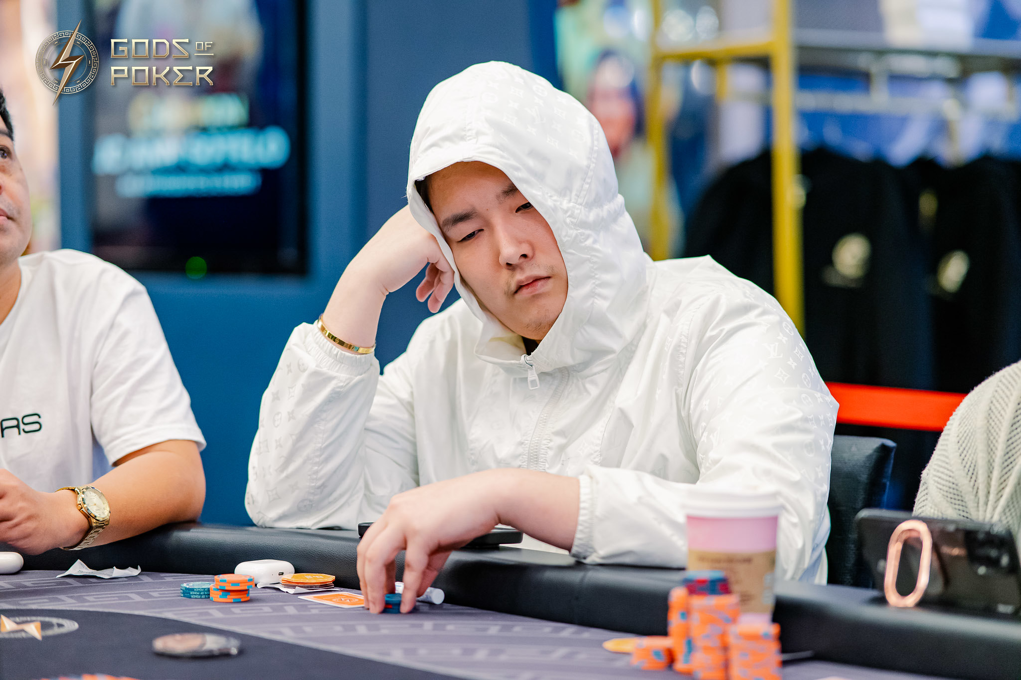 Man in white hoodie looks tired at a poker table with chips and cards.