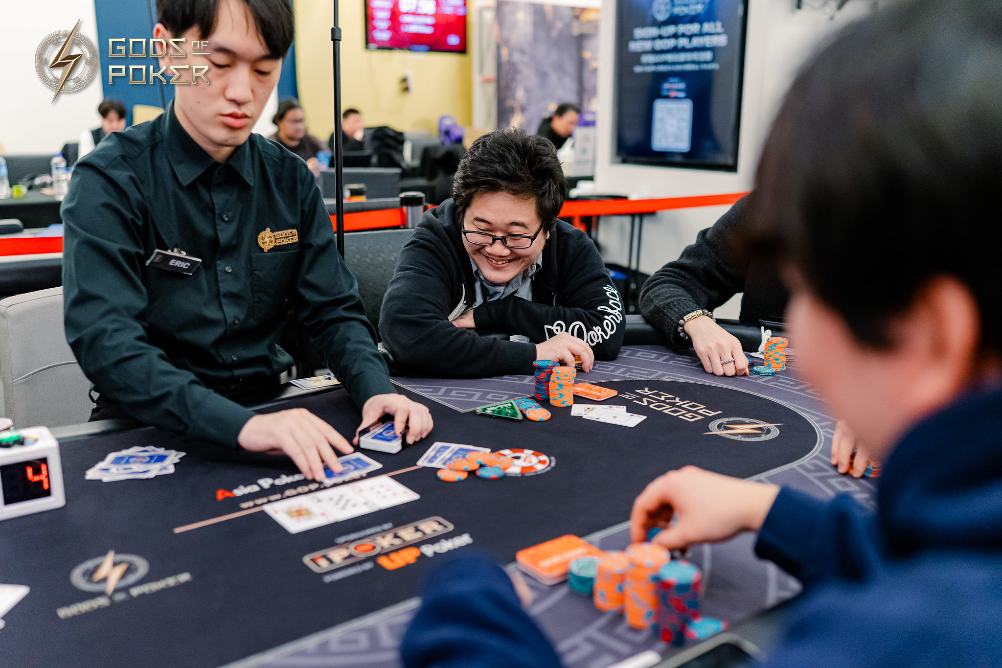Man dealing cards at a black poker table with other players and chips.