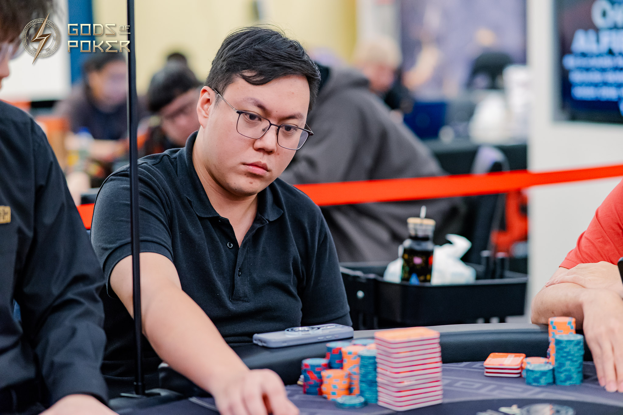 A man in glasses wearing a black shirt intently plays poker with chips on the table.