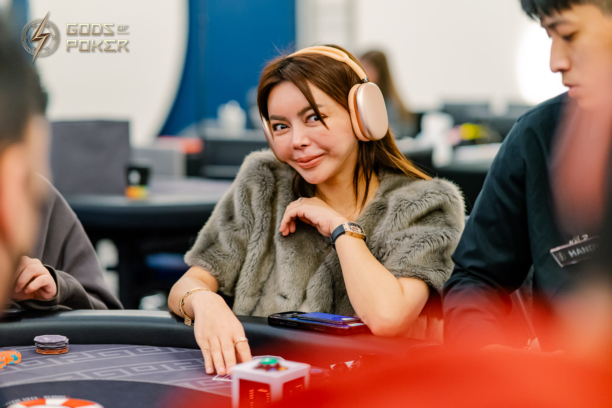 Brown-haired woman wearing headphones, smiling at a poker table with chips.