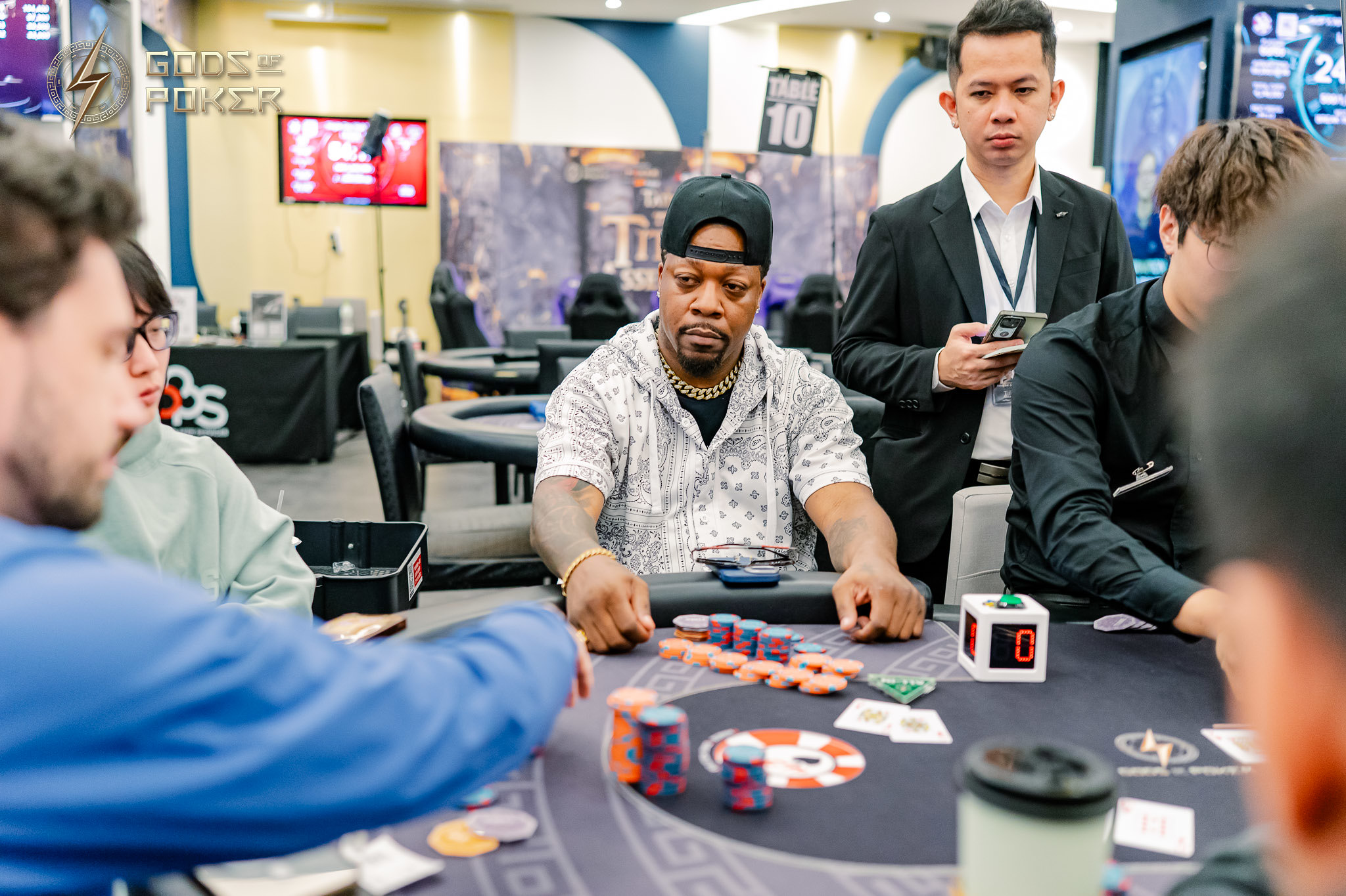 Man in cap playing poker, looking at his chips at a casino table.