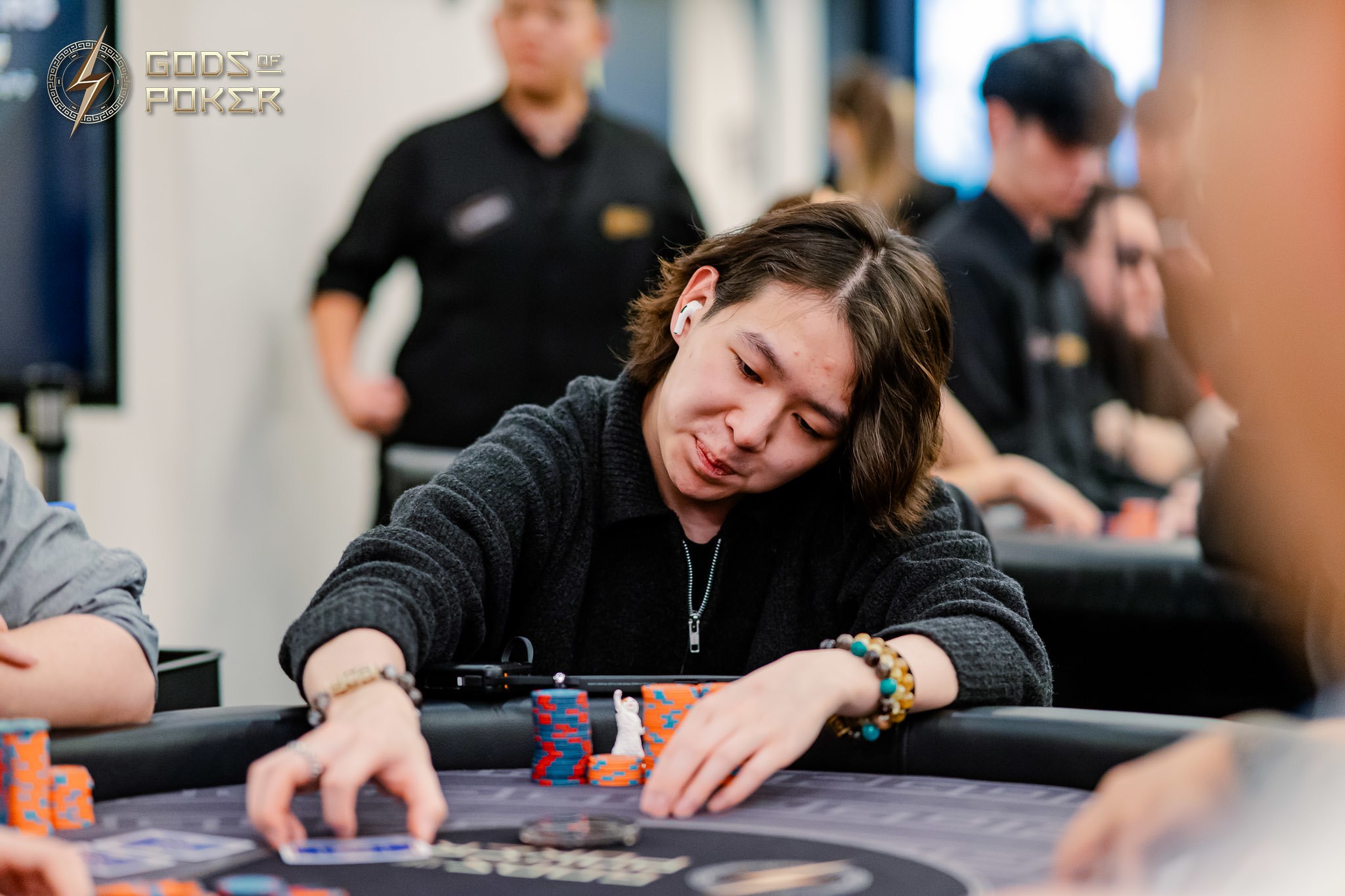 Person in black shirt intently playing poker, reaching for cards on a table with chips.