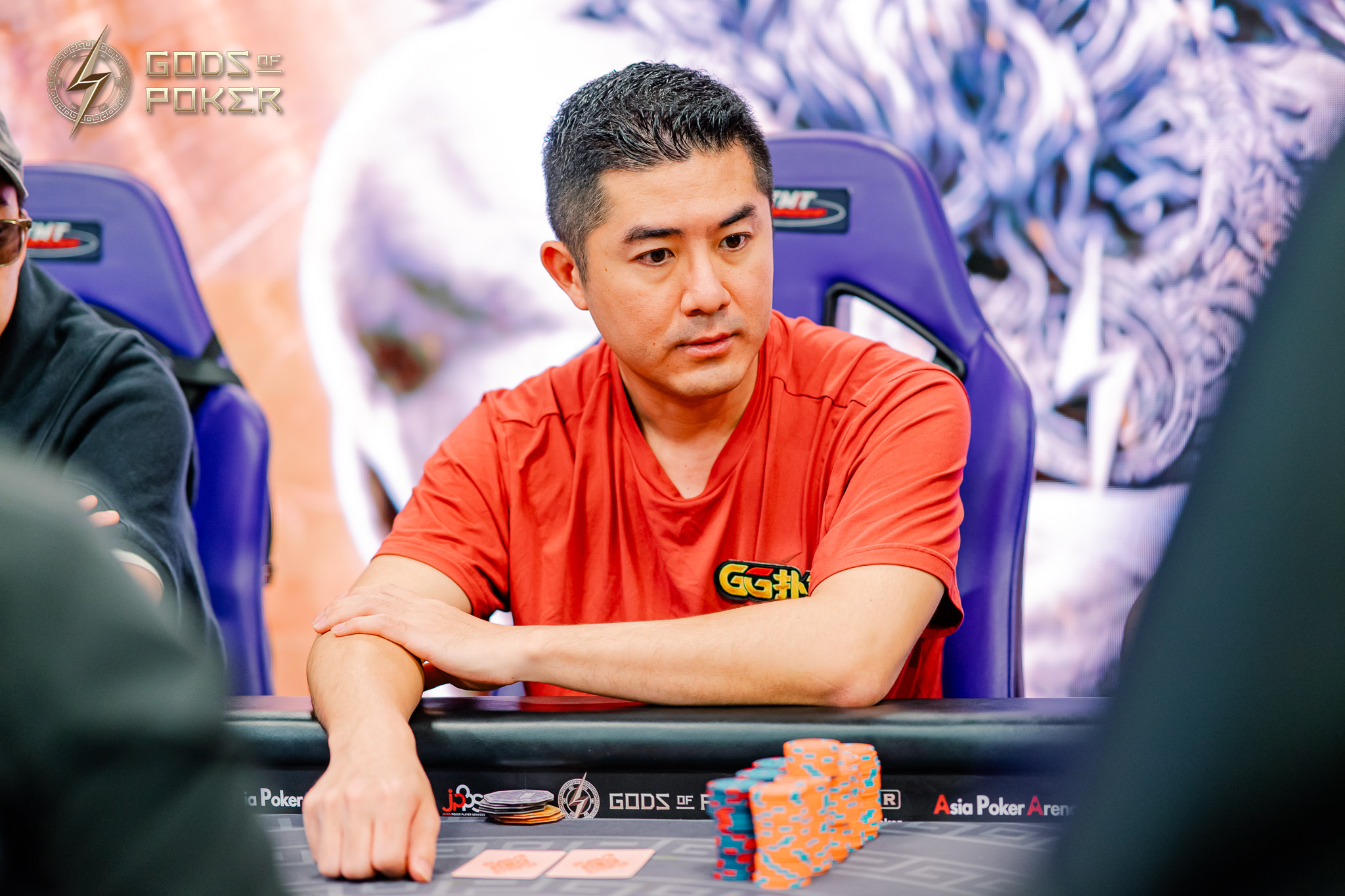 An East Asian man with a serious expression plays poker, surrounded by chips and cards.