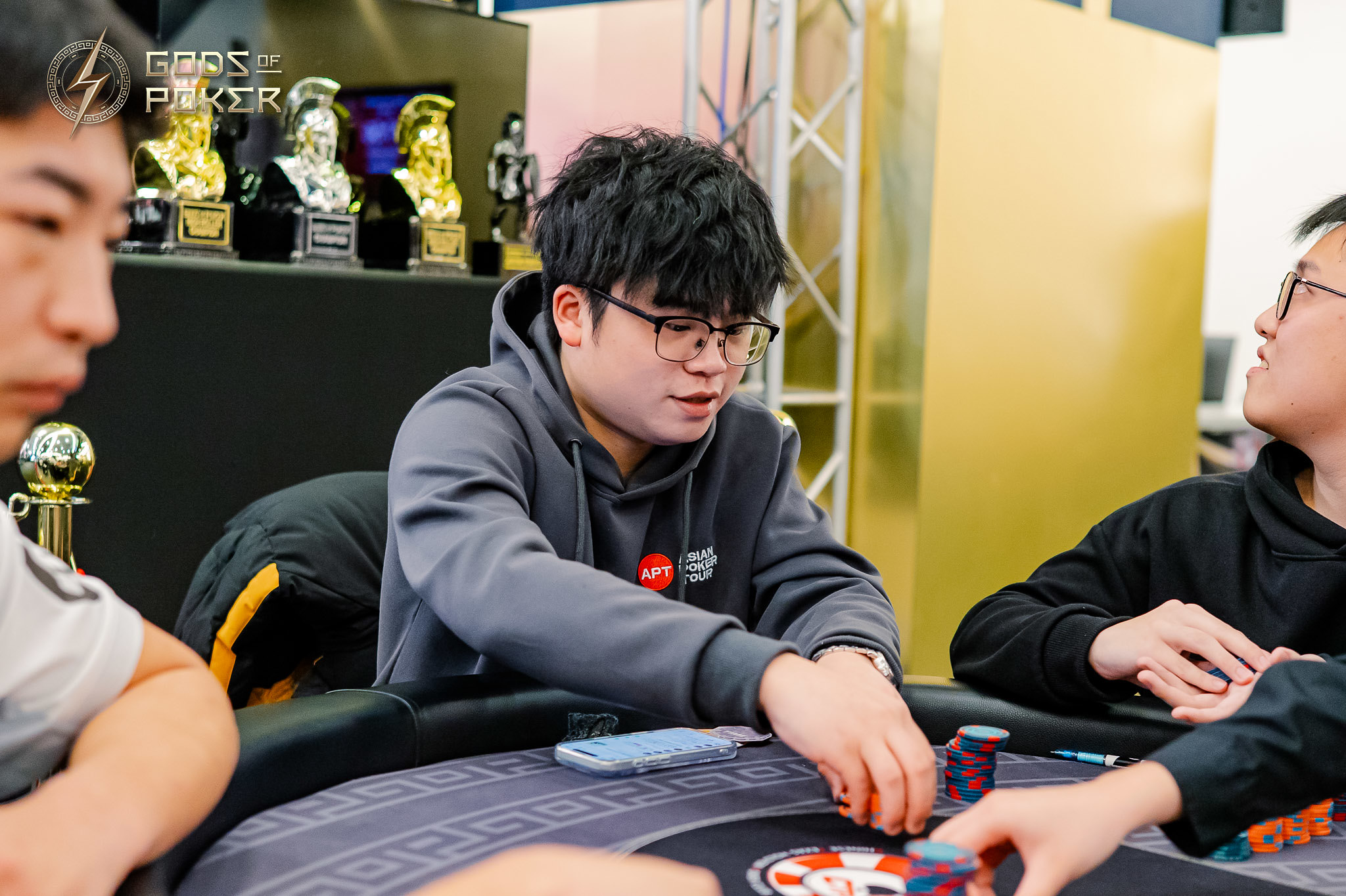 Young man with glasses in a grey hoodie moving poker chips at a casino table.