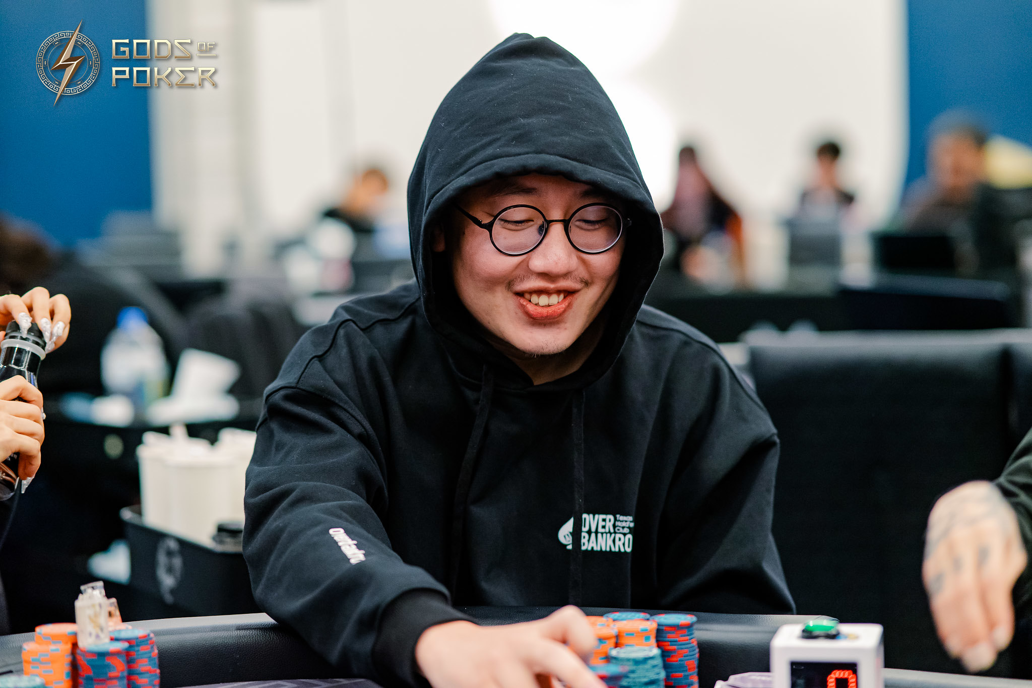 Smiling young man in black hoodie and glasses at a poker table with chips.