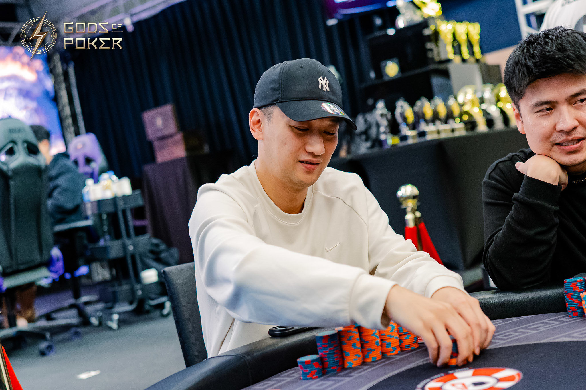 Man in a cap playing poker, moving chips on a table.