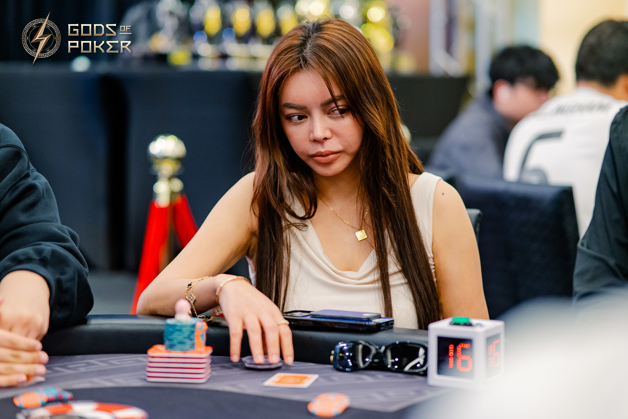 A young woman playing poker, focused on her hand at a table with chips.