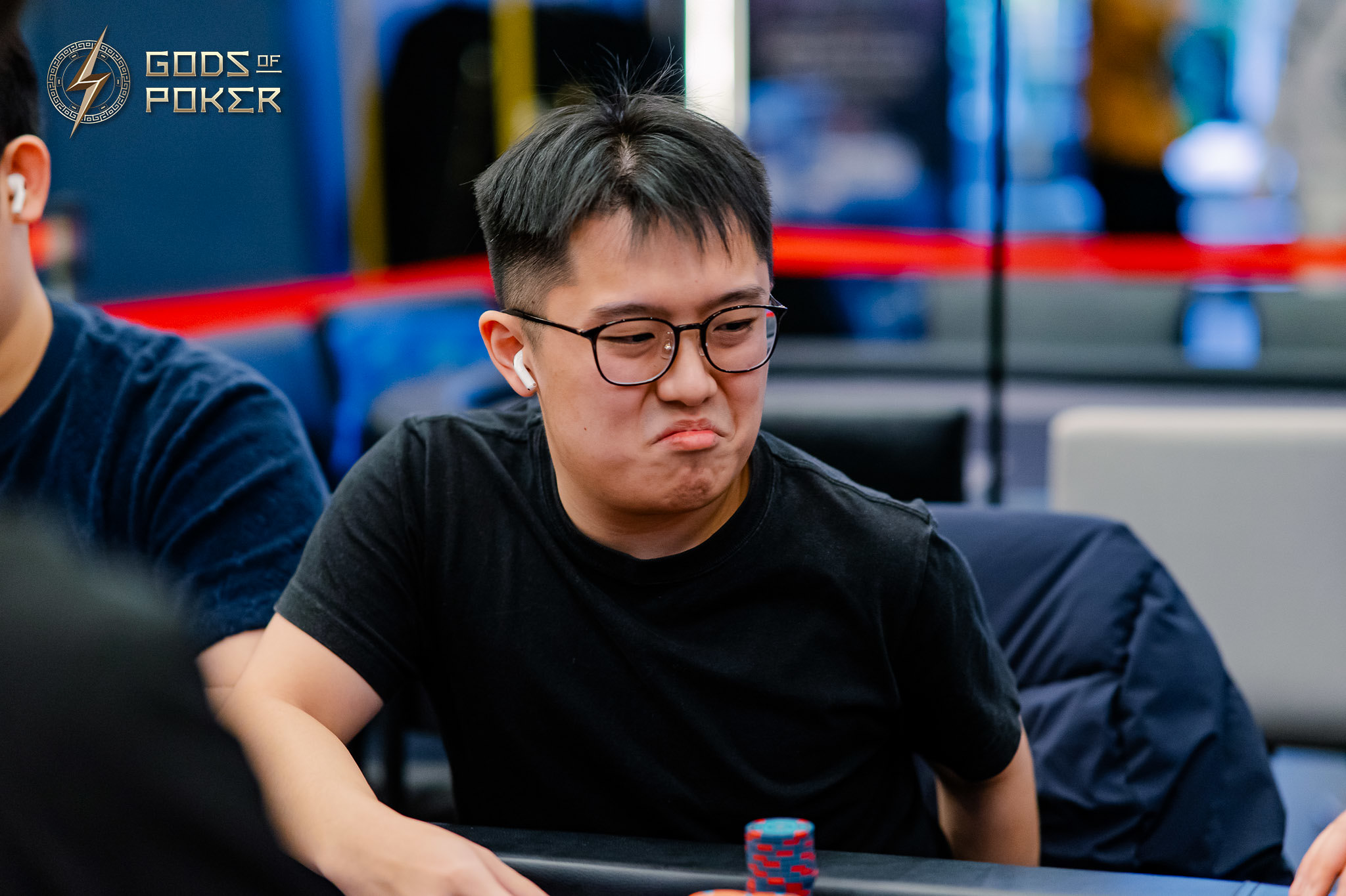 Young man with glasses making a grumpy face at a poker table.