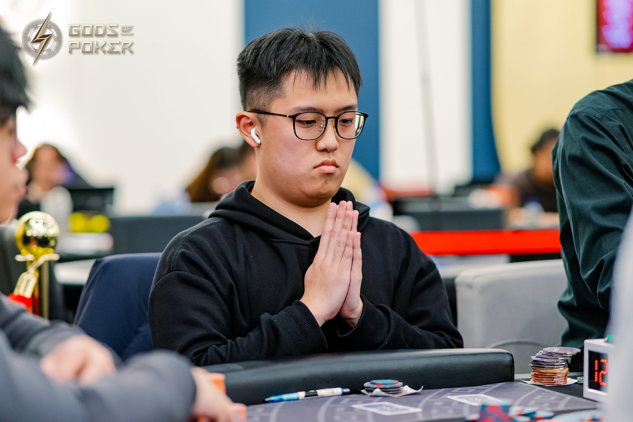Asian man in glasses praying at a poker table, deep in thought.