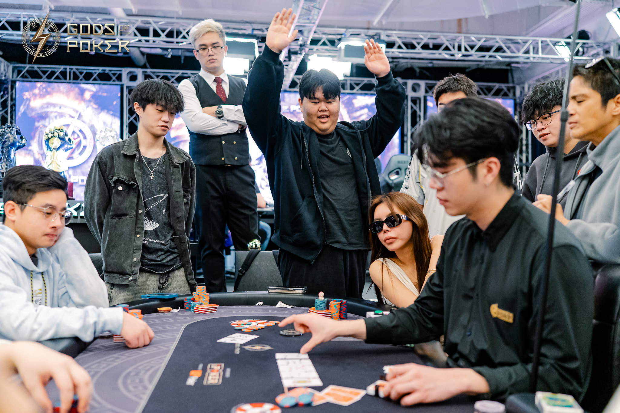 A man celebrates with raised arms at a poker table surrounded by other players.