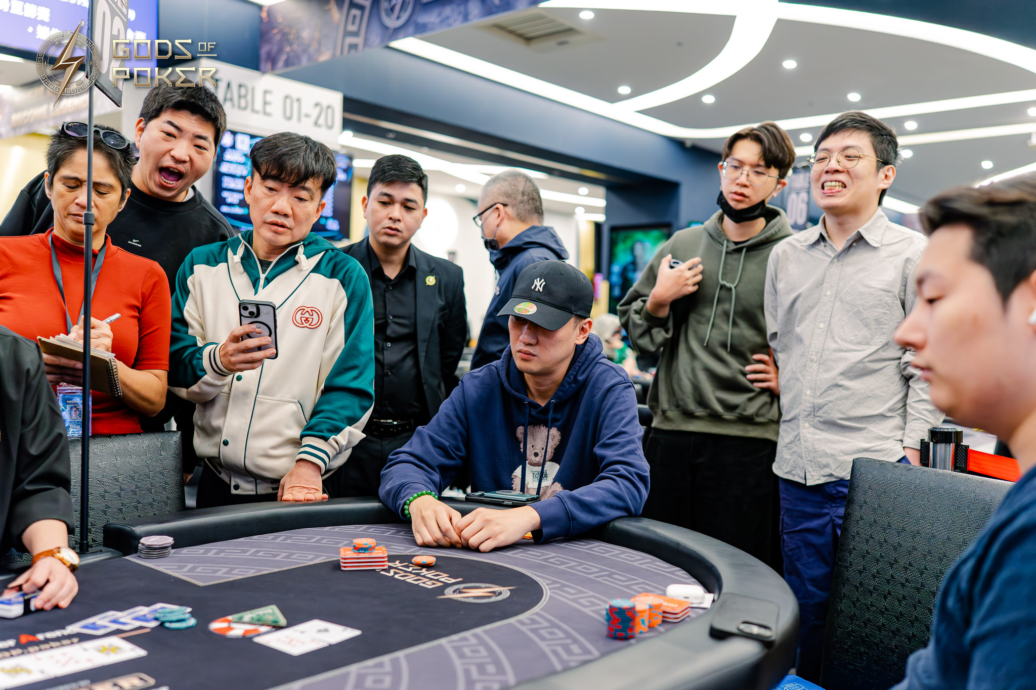 A diverse group of people intently watching a poker game at a casino table.