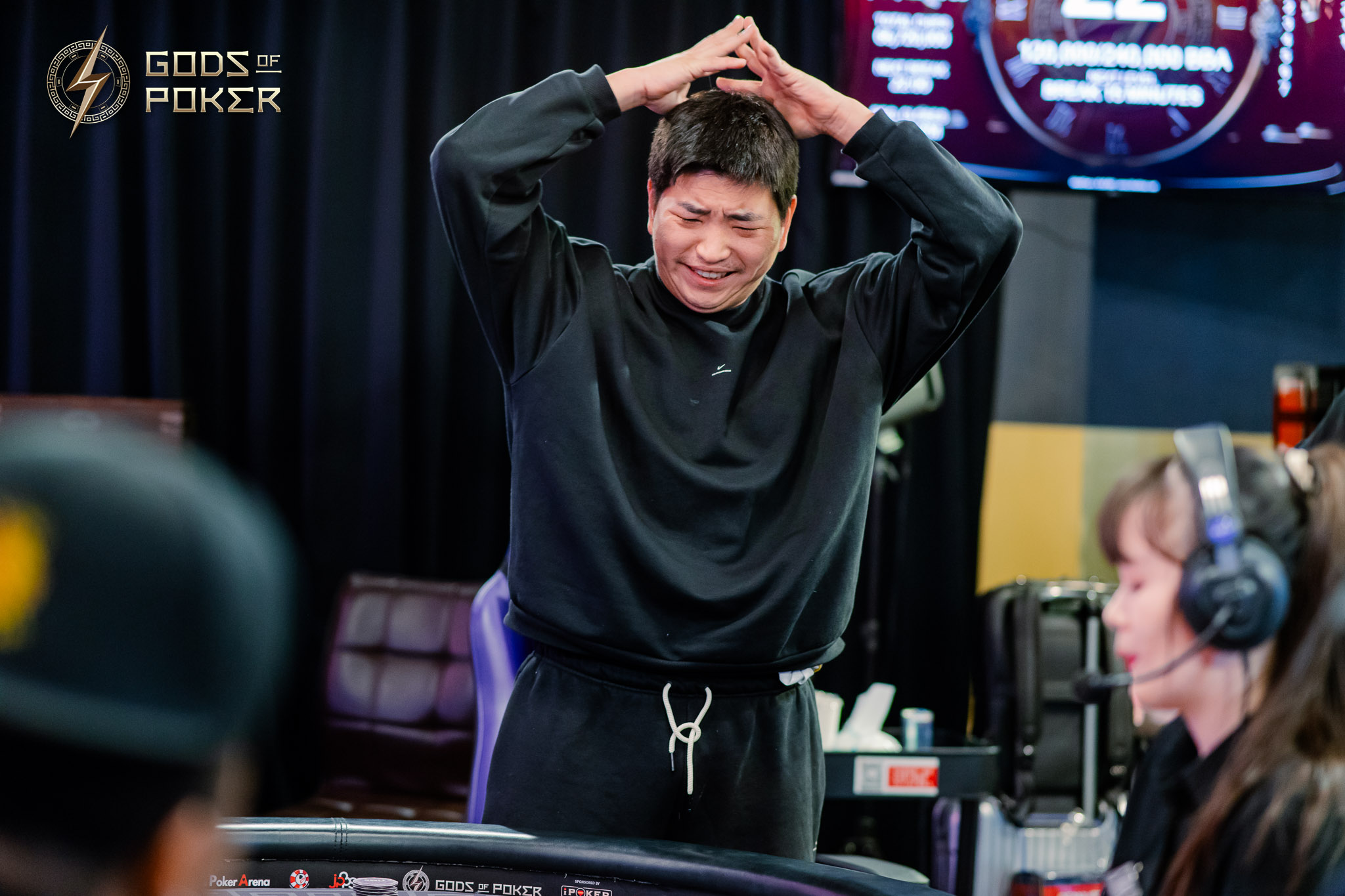 Man in black shirt with hands on head, looking distraught at a poker table.