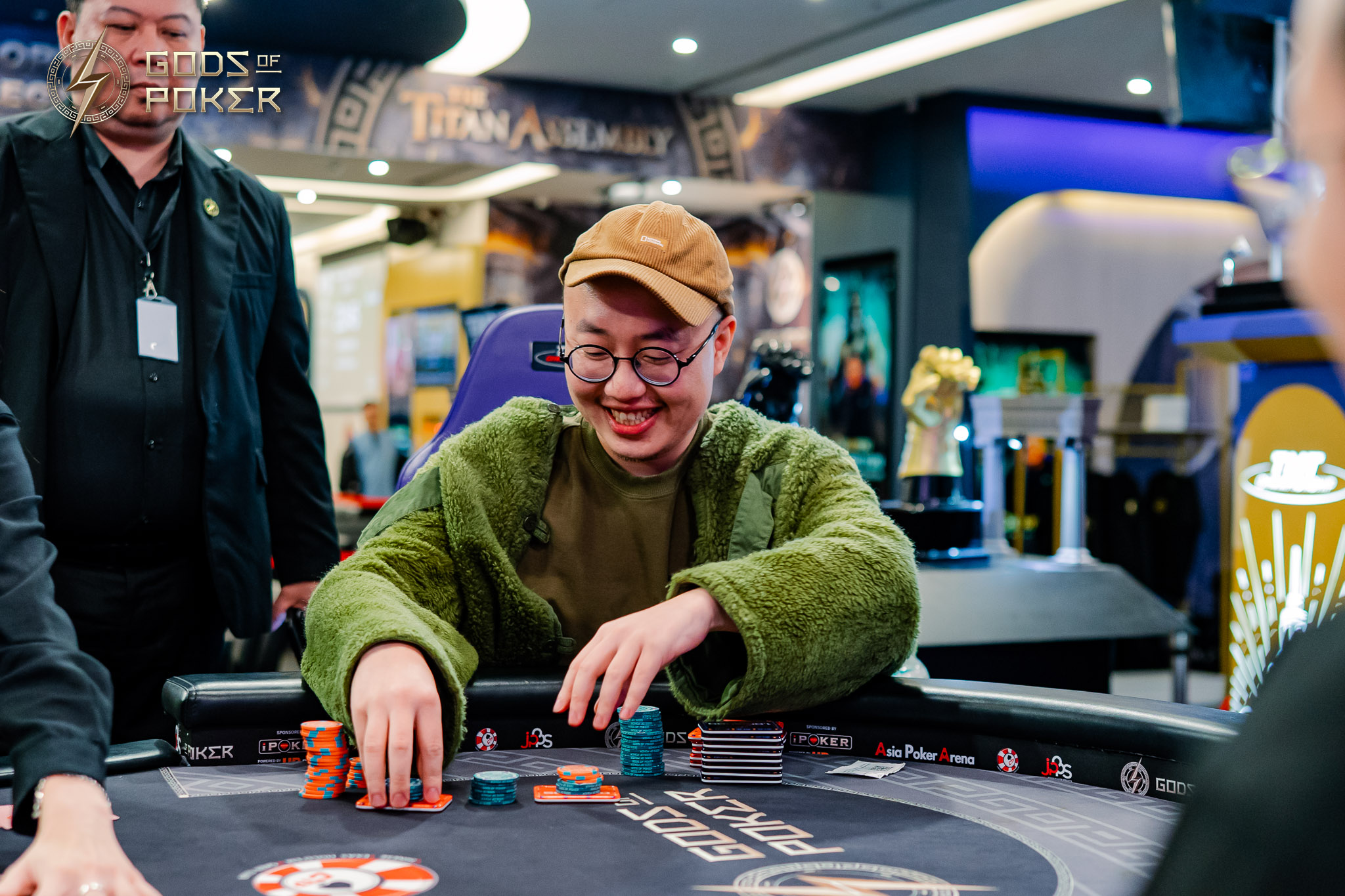 Man in a green fuzzy jacket and cap happily playing poker at a table.