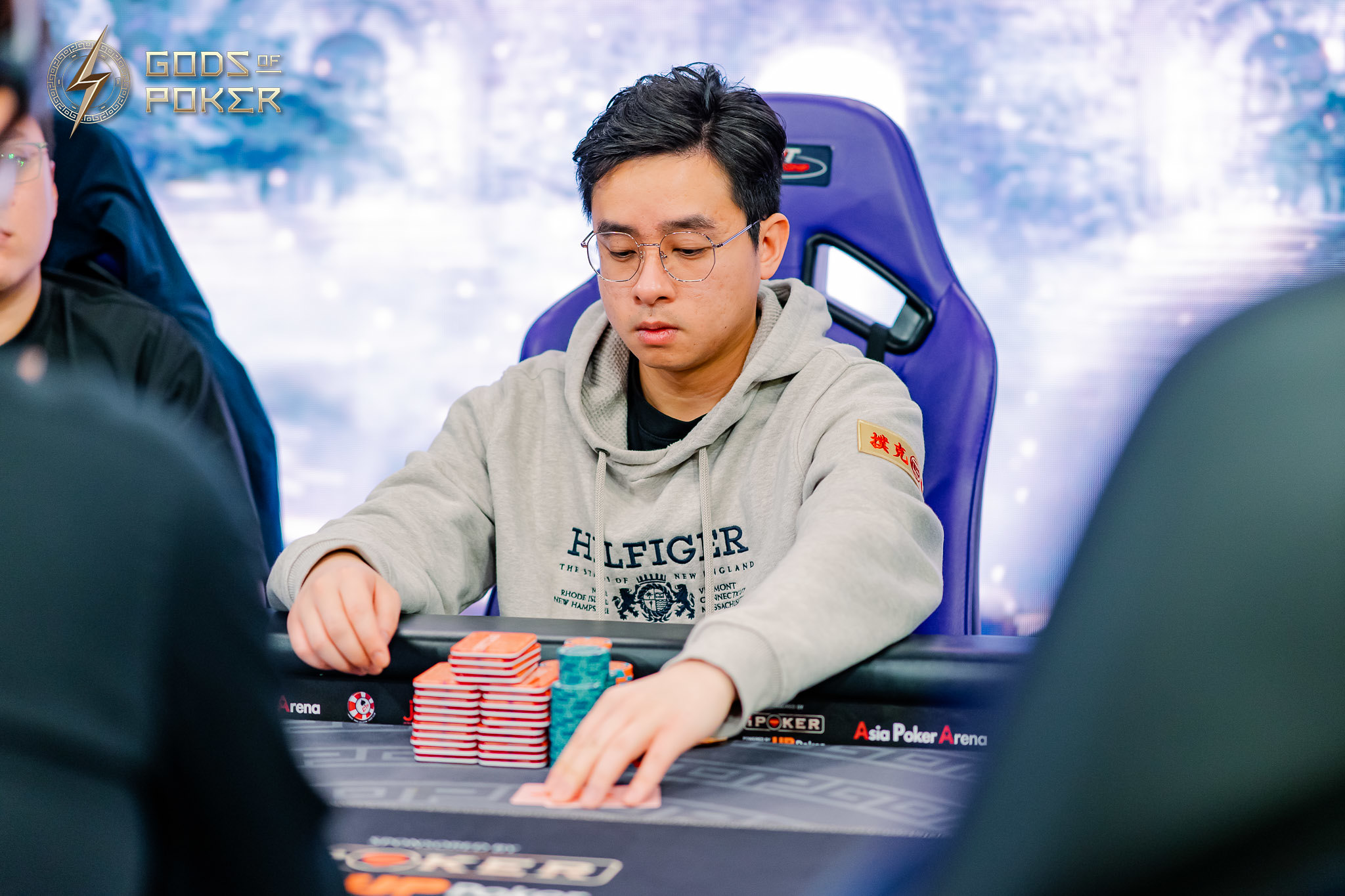 Man in glasses and grey hoodie playing poker at a table with chips.
