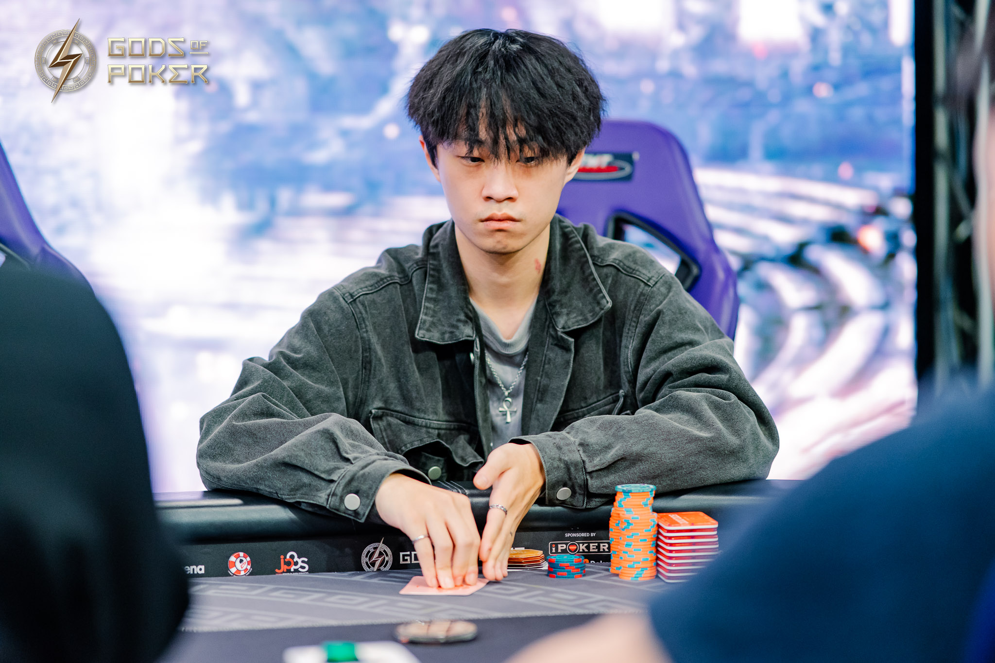 Young man with focused expression plays poker, holding cards at a table with chips.