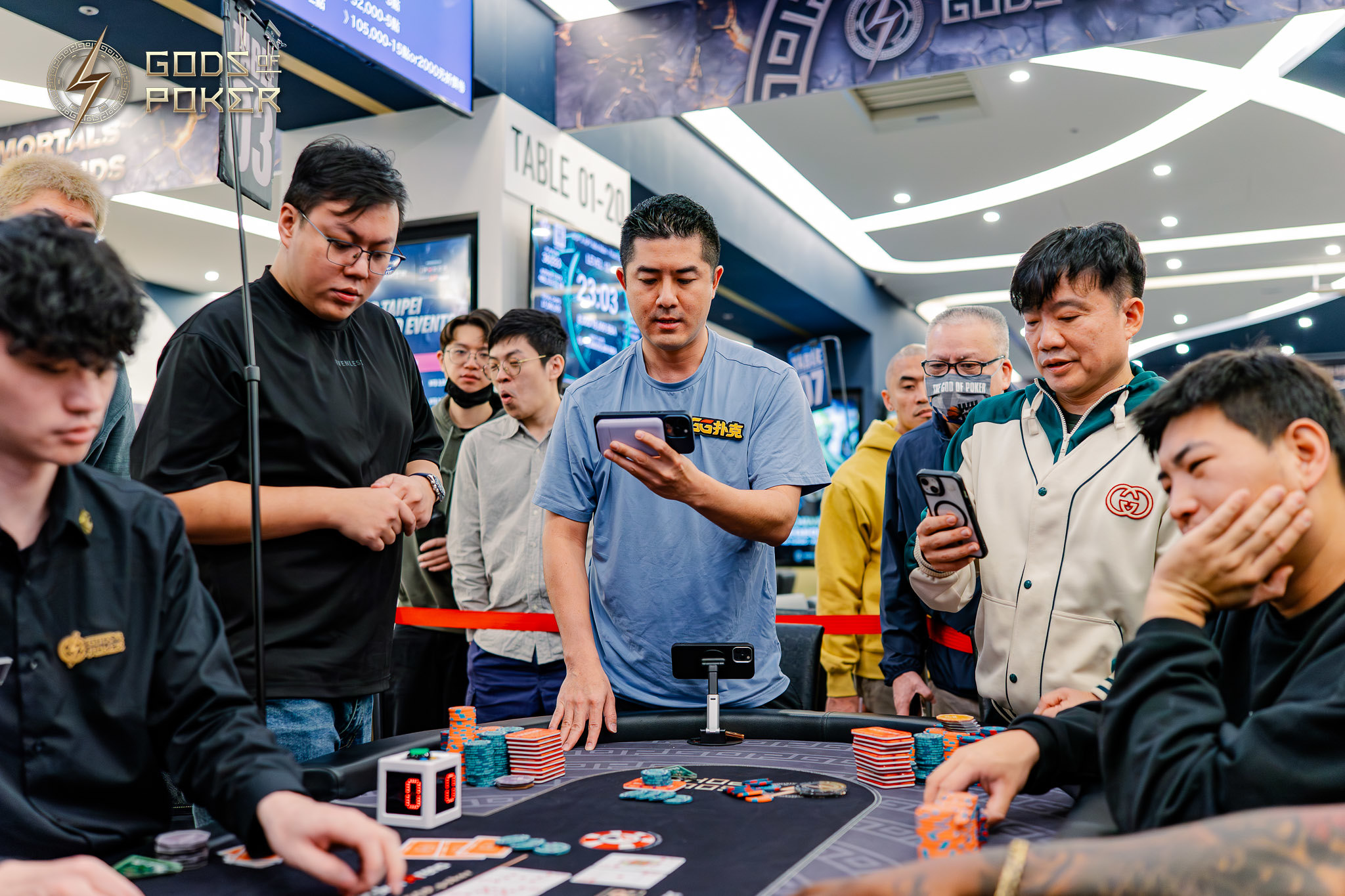 Men play poker while others watch intently at a crowded casino table.