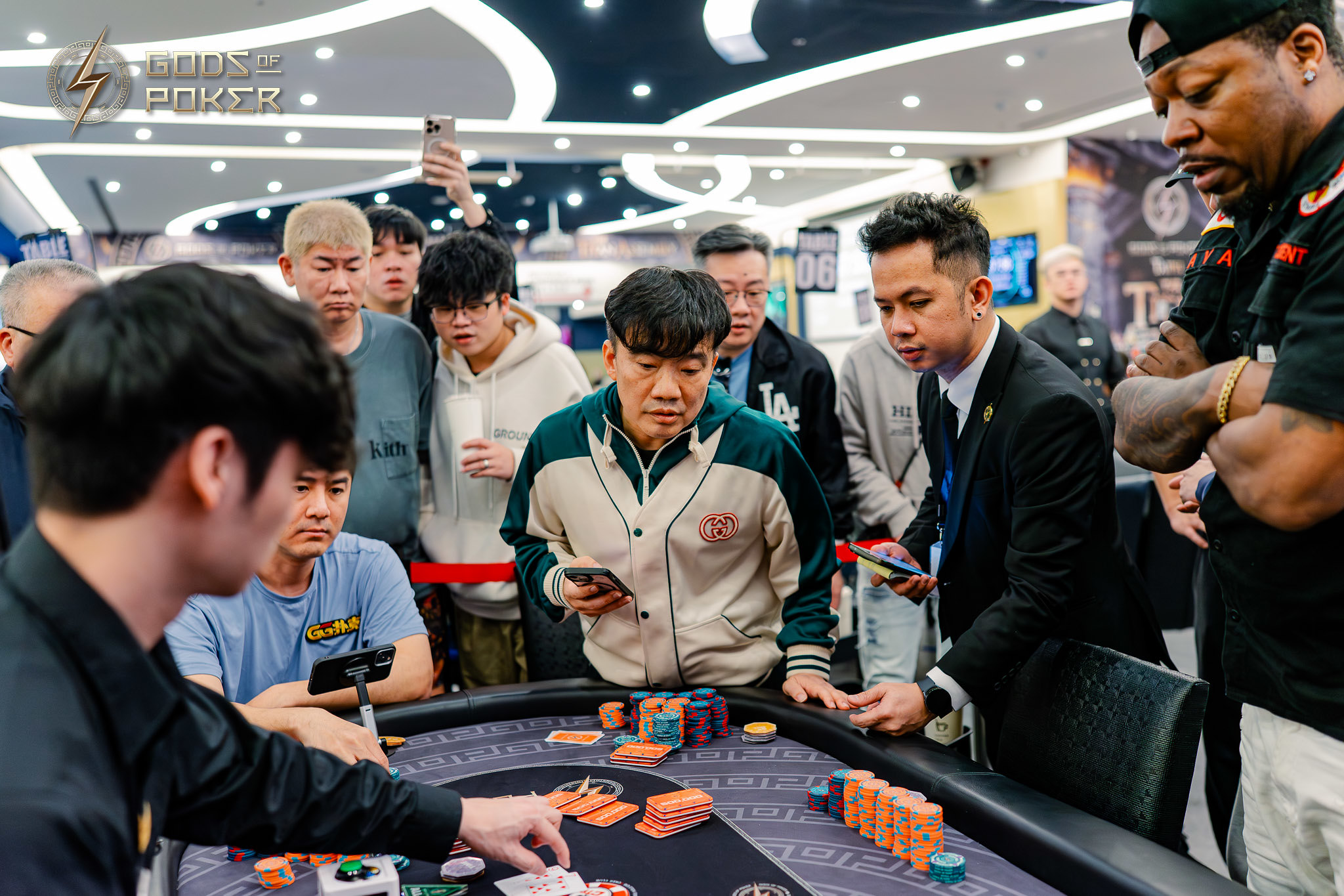Men gather around a poker table with cards and chips in a bustling casino.