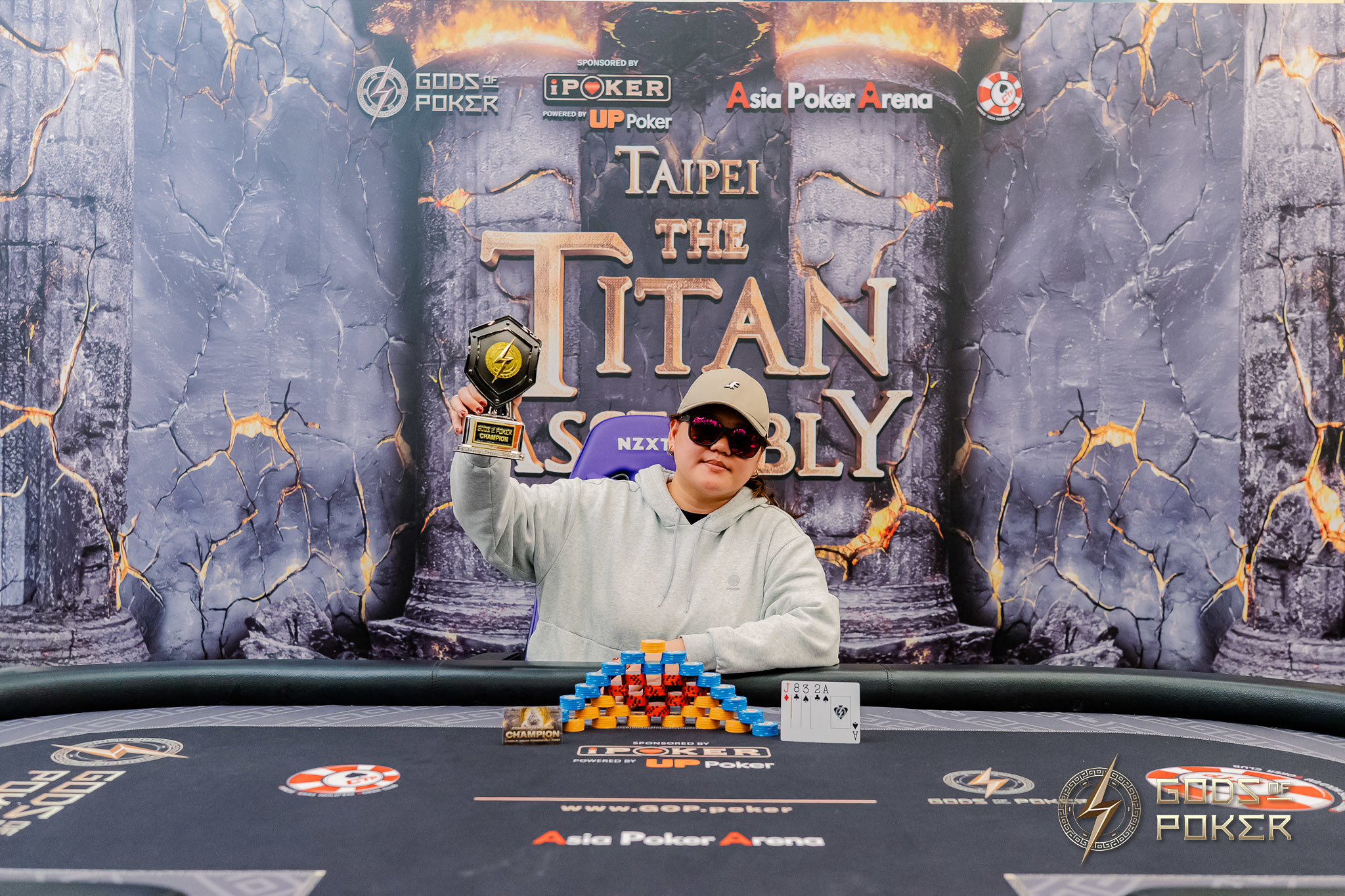 Happy winner holding a golden trophy at a poker table, 'Taipei Titan Assembly' banner.