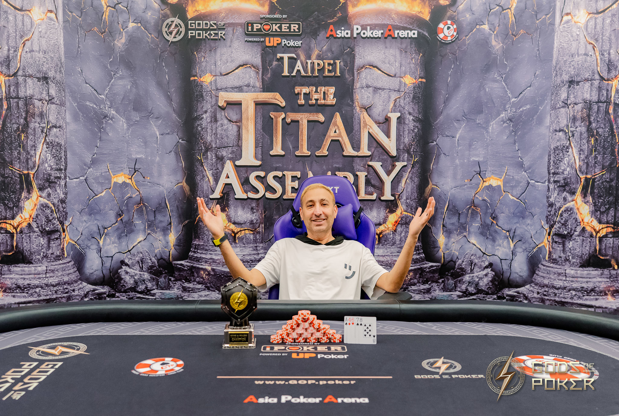 Young man with arms raised celebrates a poker tournament victory with a trophy and chips.