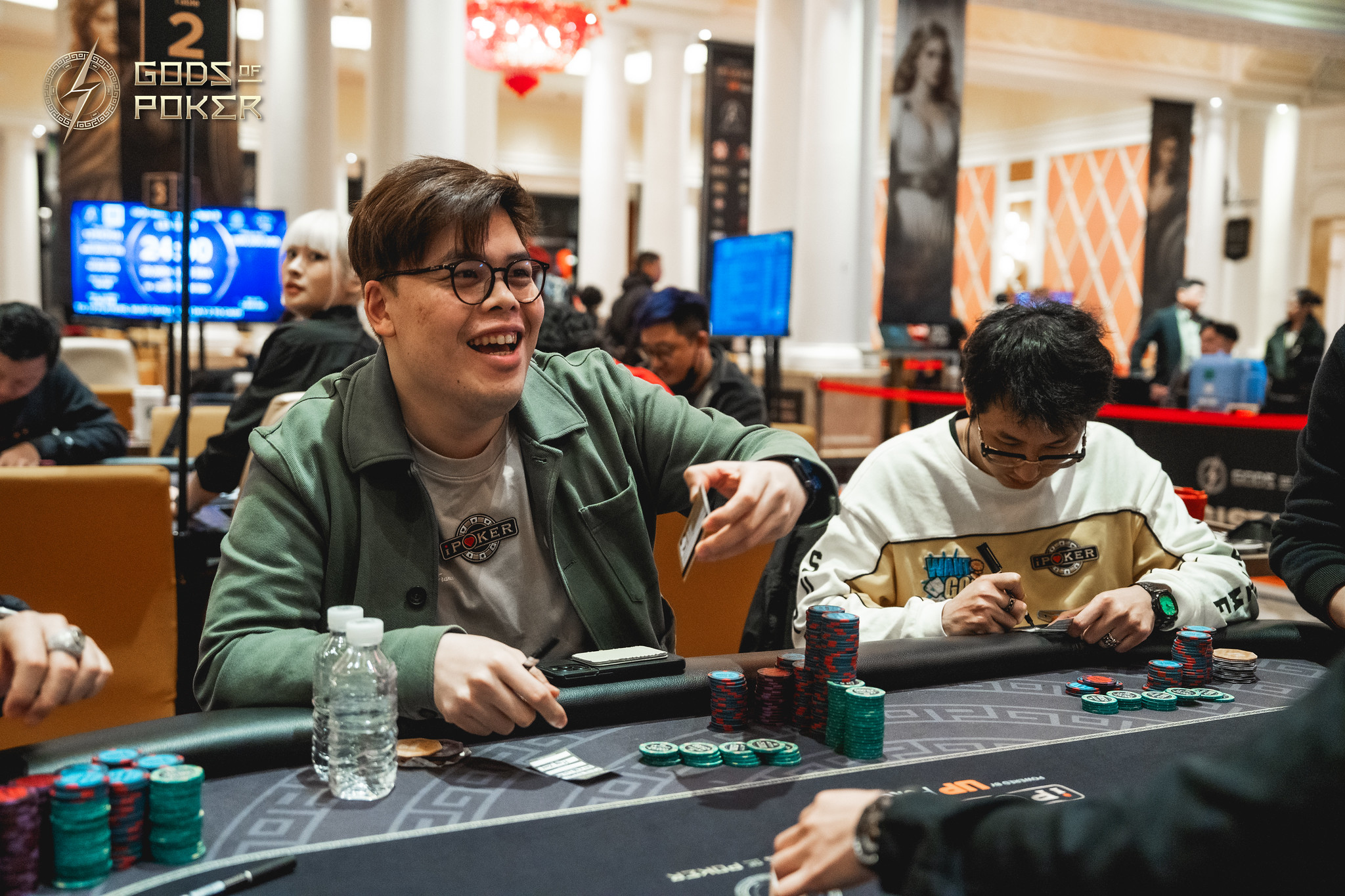 Man in green jacket smiling and laughing at a poker table with chips.