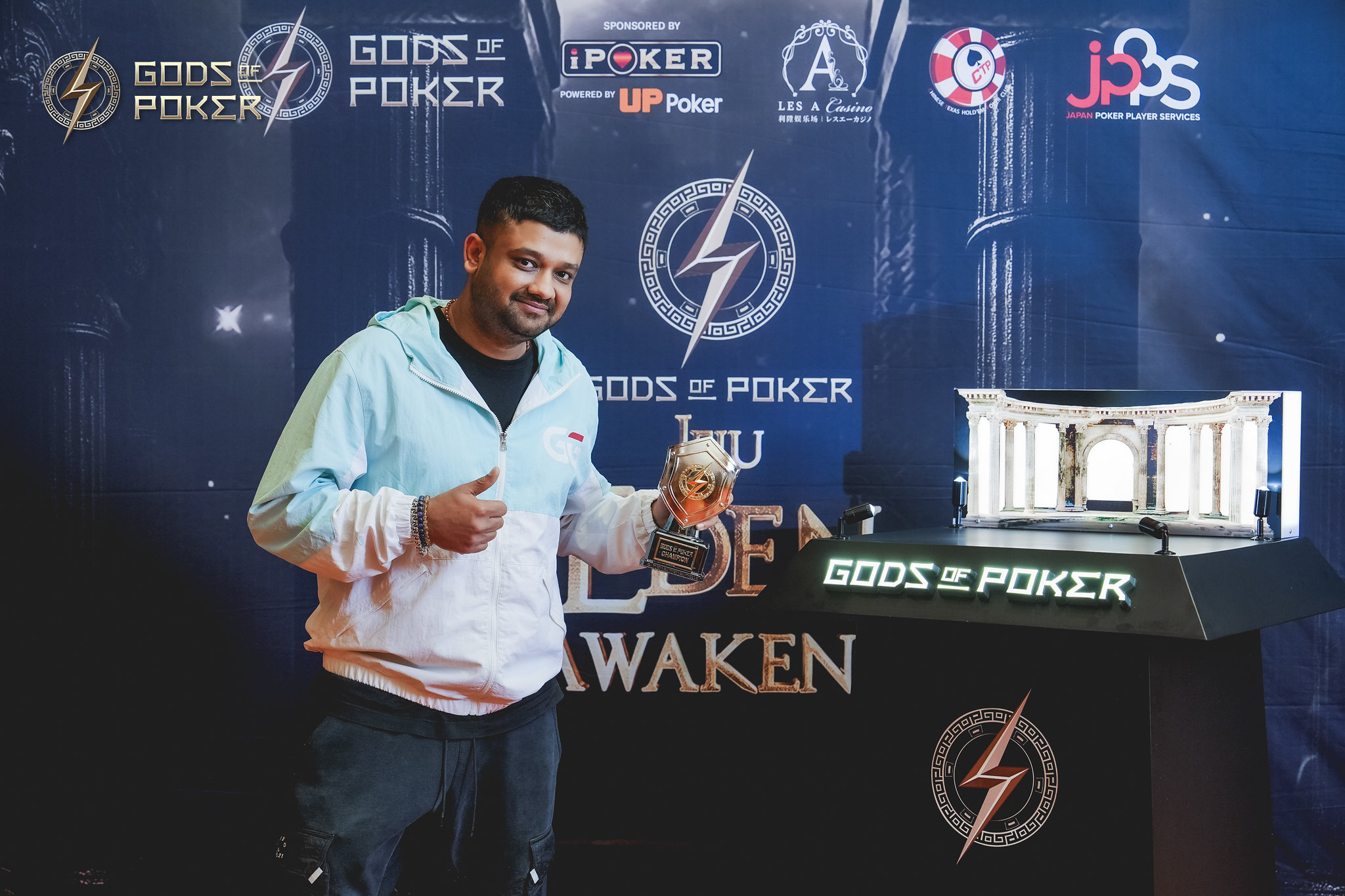 A smiling man gives a thumbs up, holding a trophy at the Gods of Poker event.