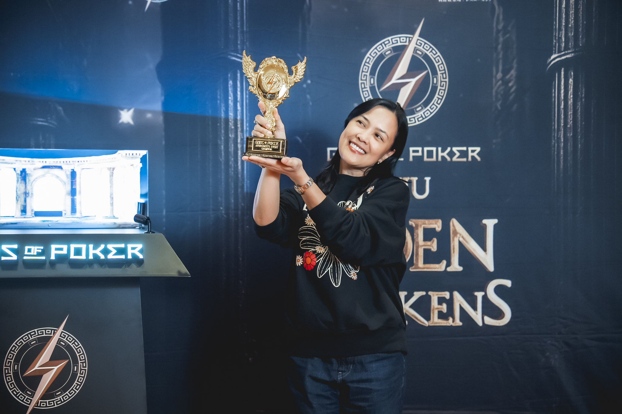 A smiling woman in a black shirt proudly holds a golden winged trophy.