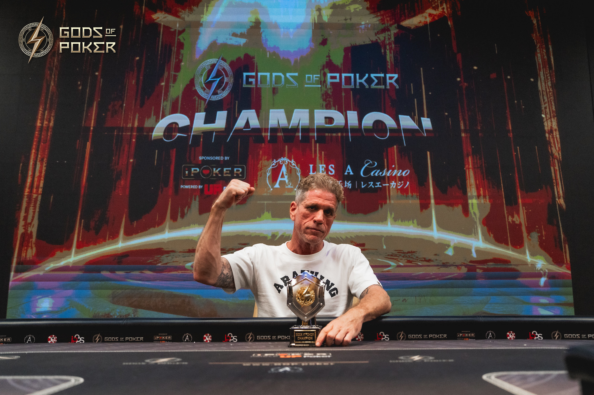 Poker champion raises his fist in victory before a 'Gods of Poker Champion' screen.
