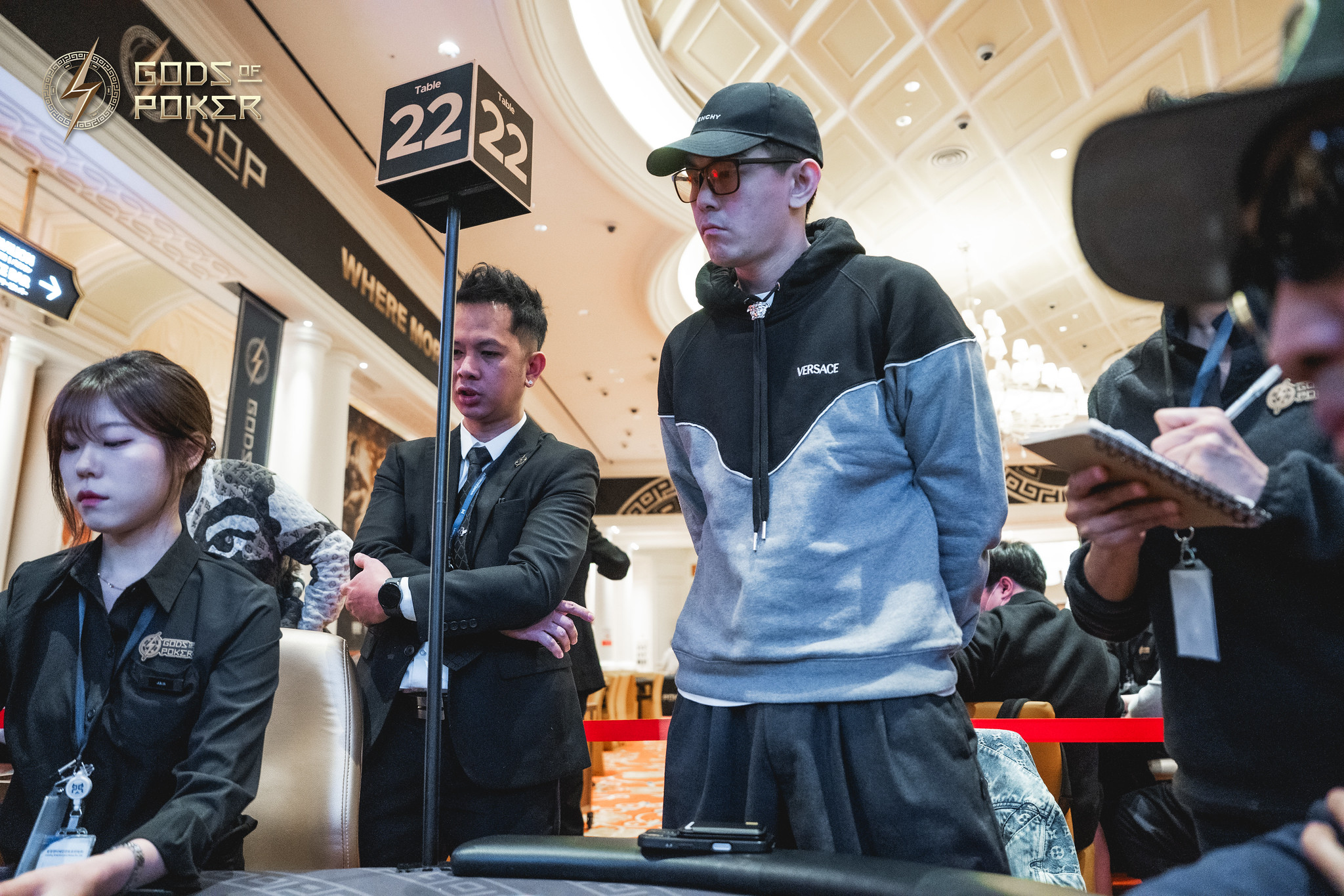 Man in a cap and hoodie watches intently at a bustling casino event.