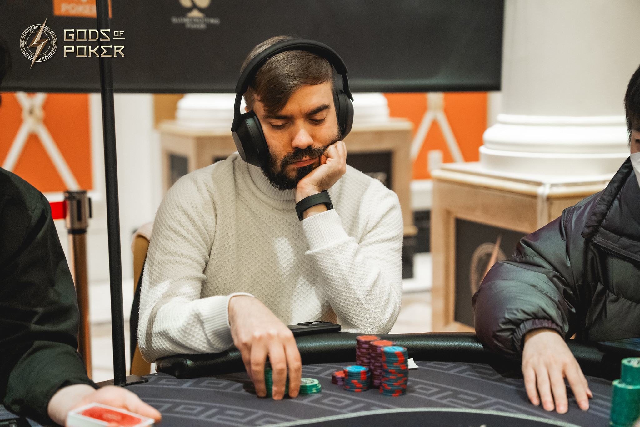 A man in headphones, wearing a turtleneck, intently watches his poker chips at the table.