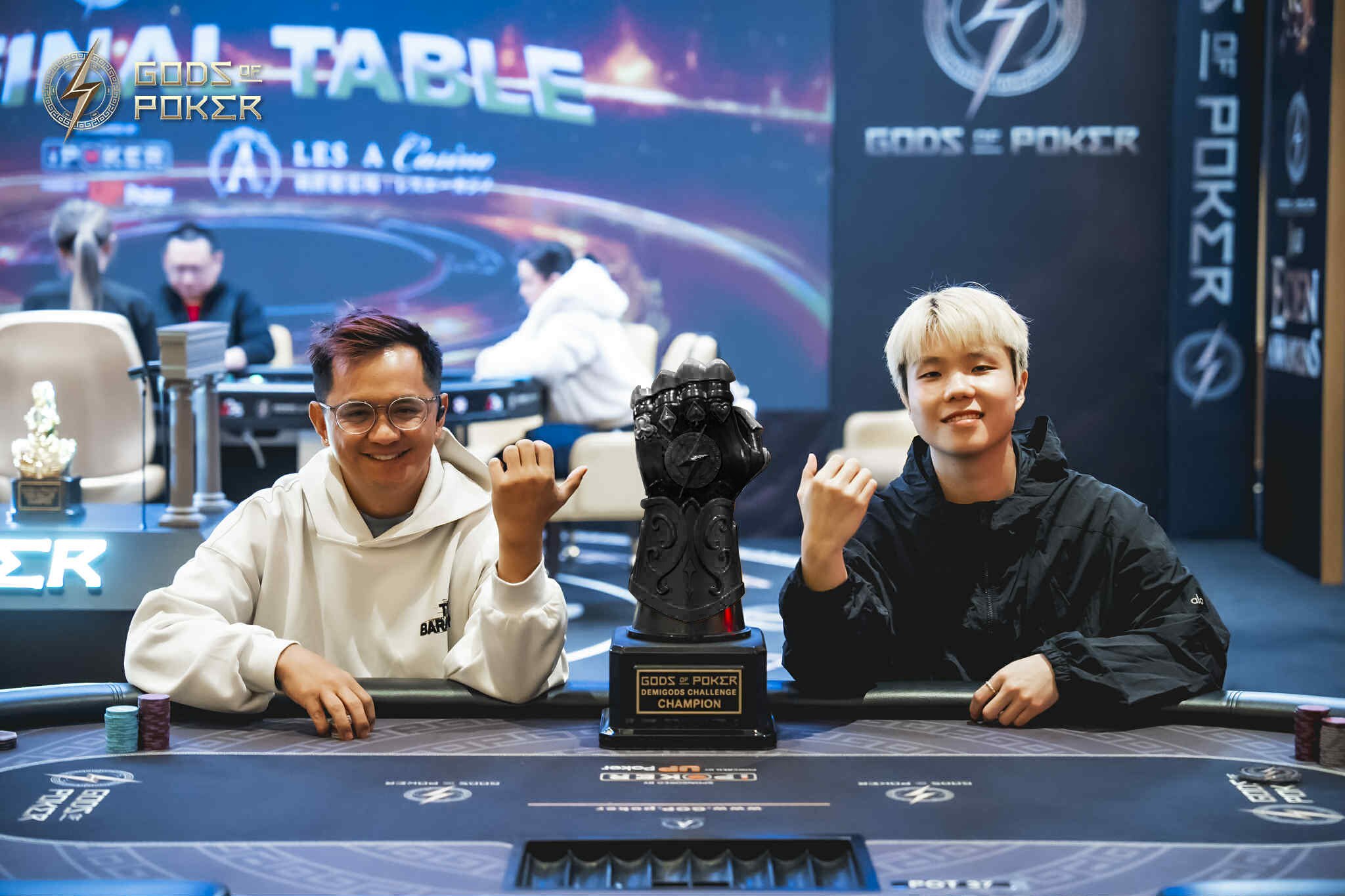 Two smiling men celebrate their poker tournament victory with a trophy.